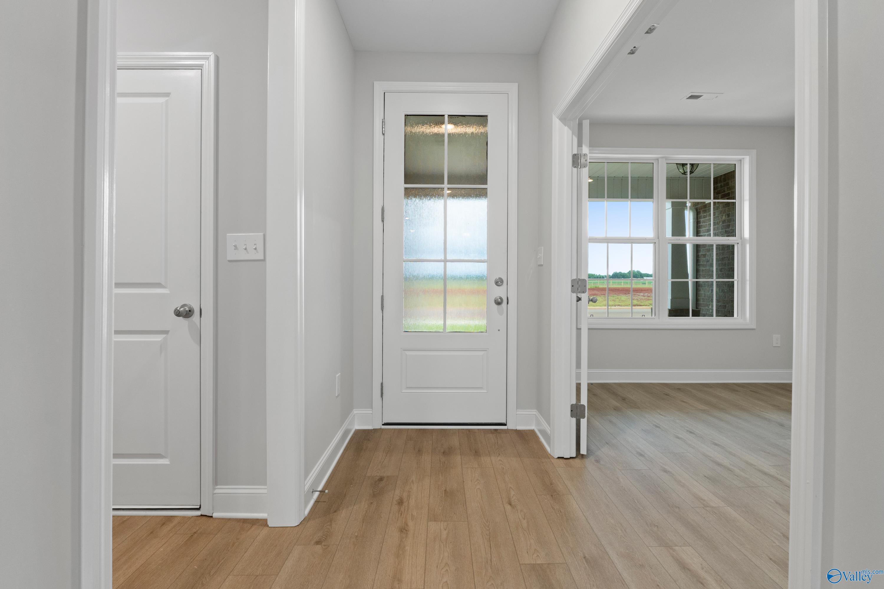 Bright entry hallway with hardwood floors, white doors, and scenic outdoor view through glass front door in The Rockford B home, Toney, Alabama