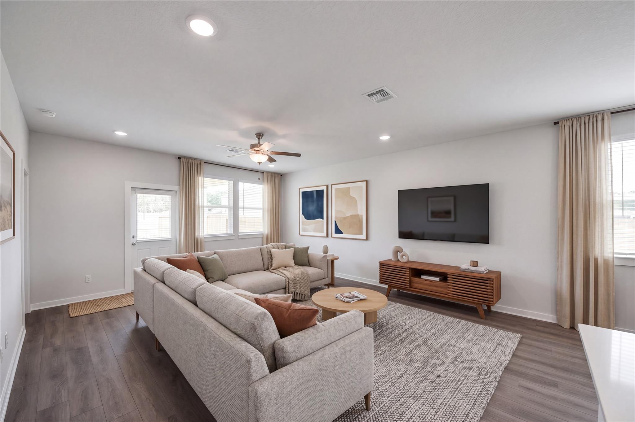 Bright living room with sectional sofa, wood-look flooring, and mounted TV in Davidson Homes The Brazos F, Cleveland, Texas