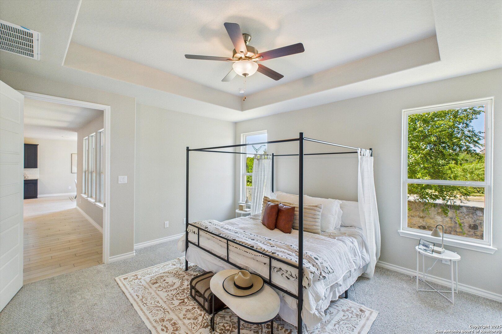 Elegant canopy bed with white bedding and pillows in serene master bedroom, ceiling fan, tree views via windows, Davidson Homes The Jennings H in Ladera, San Antonio
