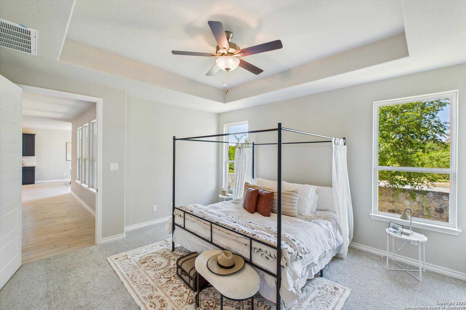 Elegant canopy bed with white bedding and pillows in serene master bedroom, ceiling fan, tree views via windows, Davidson Homes The Jennings H in Ladera, San Antonio
