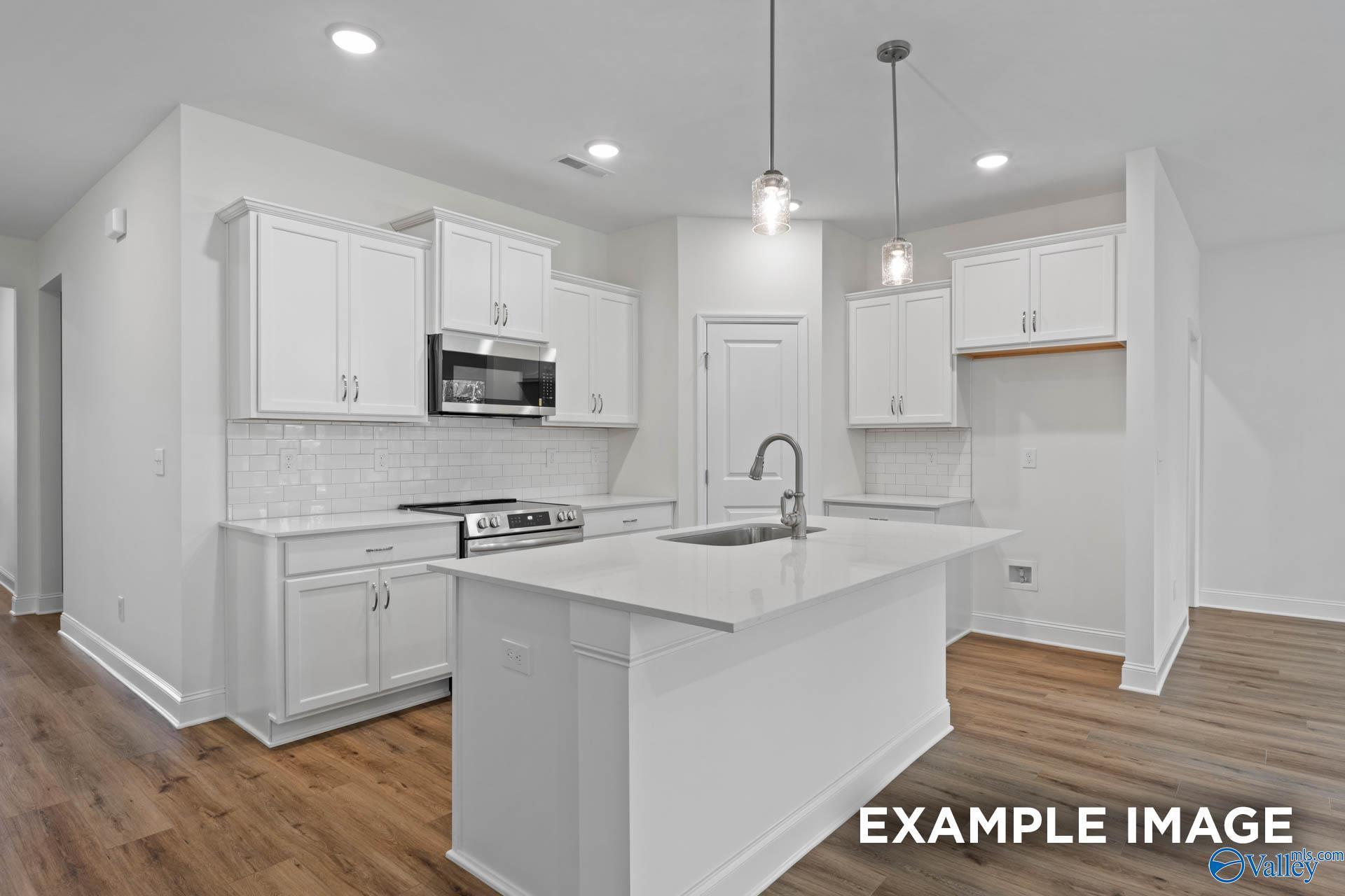 Modern white kitchen with large island, stainless steel appliances, subway tile backsplash in Evermore Homes Daphne E, Harvest AL