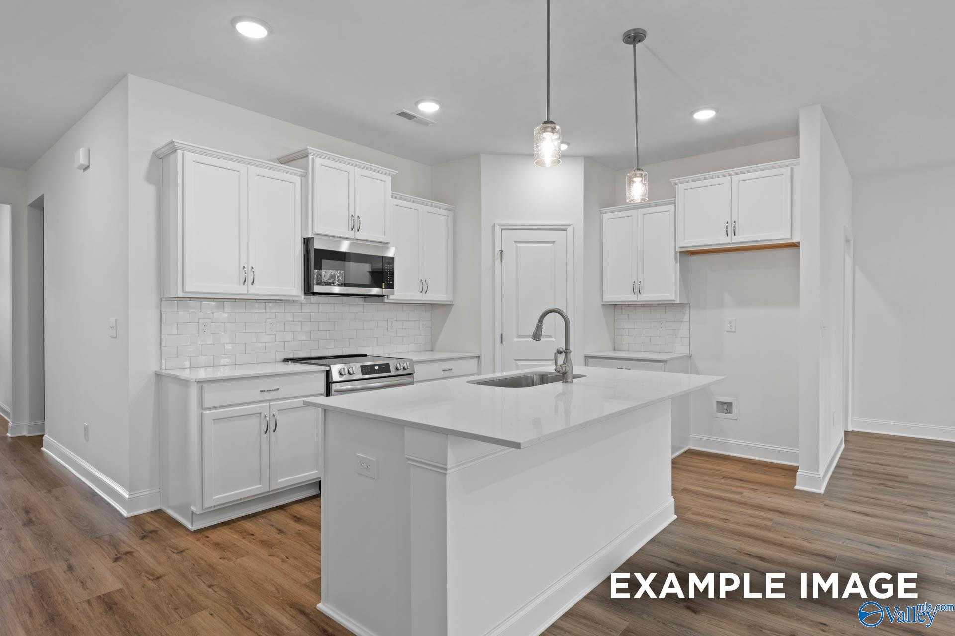 Spacious modern kitchen with white cabinets, stainless steel appliances, quartz island sink, subway tile backsplash in Davidson Homes The Daphne D, Athens, AL