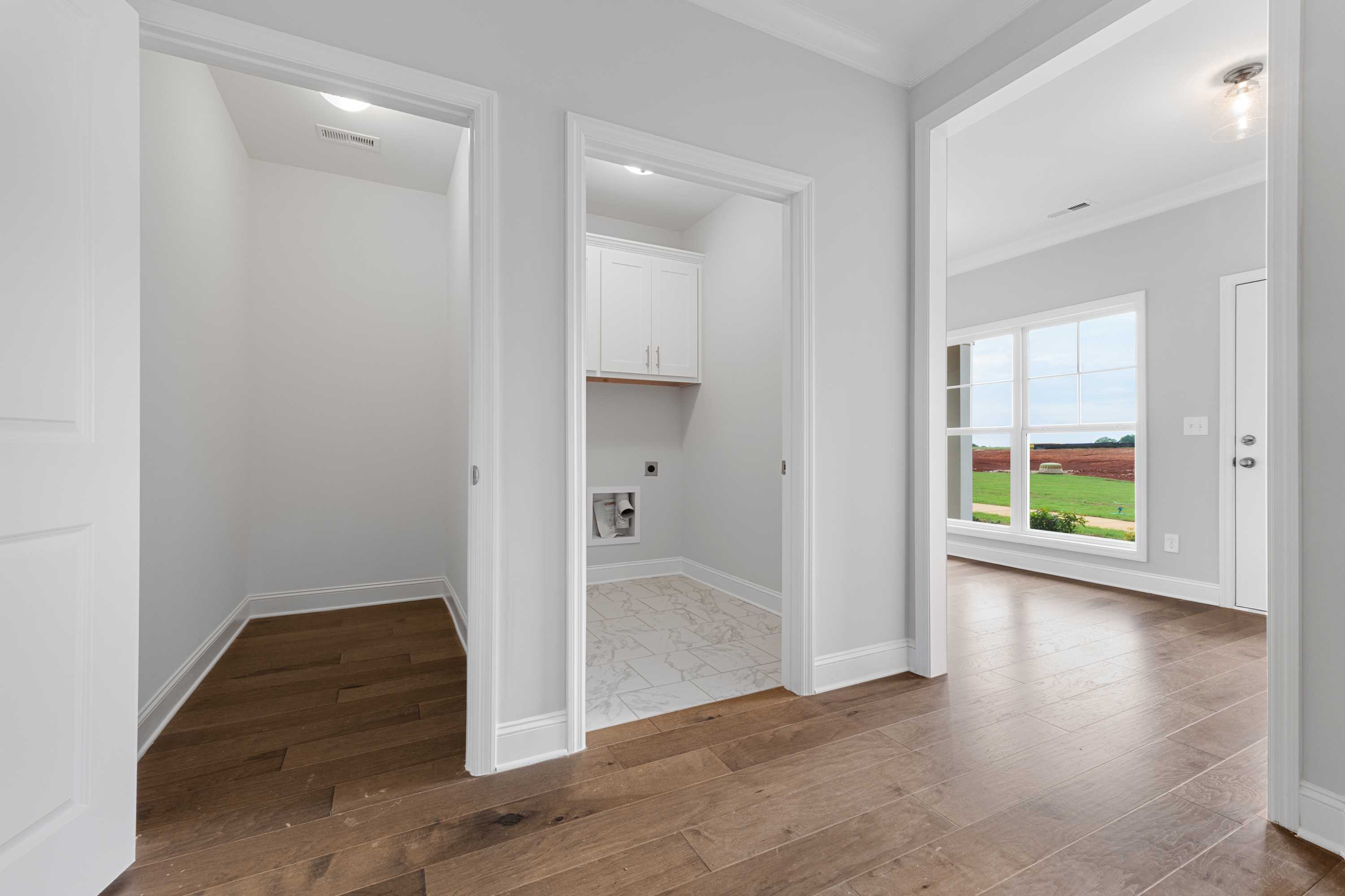 Spacious laundry room in The Copeland B featuring white cabinets, tiled floor, washer-dryer space, and hardwood hallway with window view