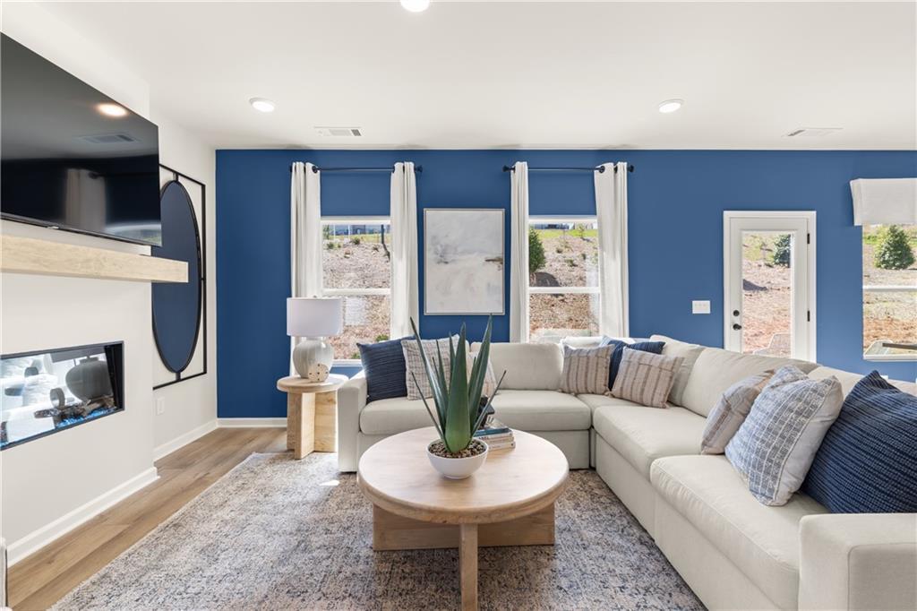Modern living room featuring blue accent wall, gas fireplace, L-shaped white sofa, and large windows in Davidson Homes The Burton C, Canton, Georgia