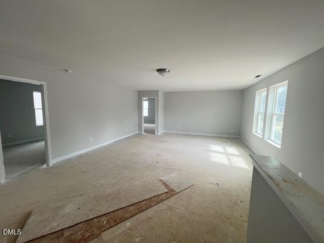 Spacious unfinished upstairs room with gray walls, large windows, doorways, and plywood subfloor in 4-bedroom Adalynn B home, Lillington, NC
