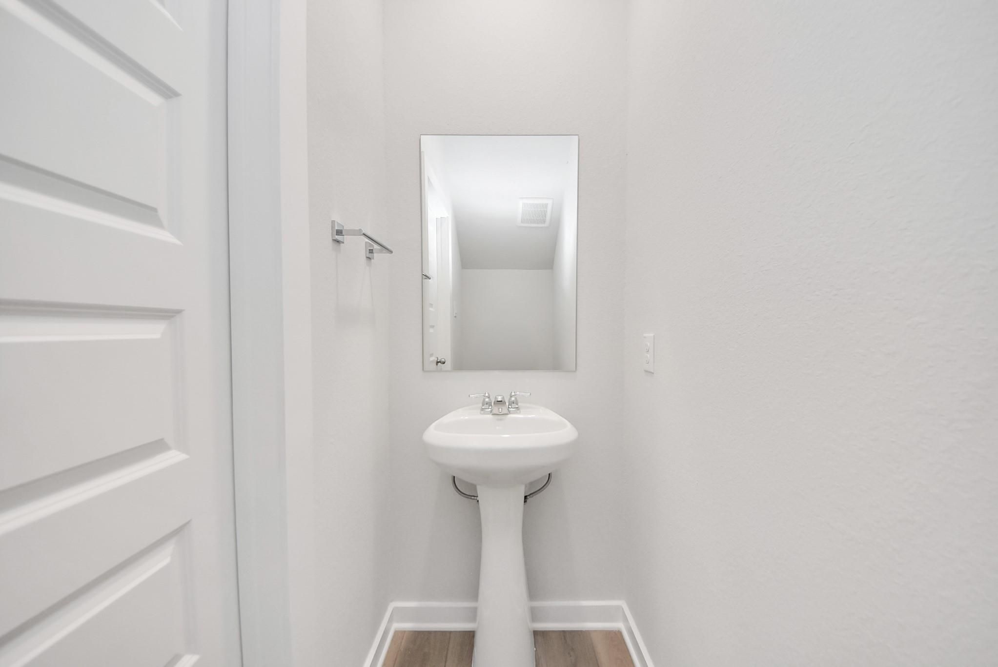 Modern half bathroom with pedestal sink and mirror in The Blanco F floor plan by Davidson Homes in Conroe, Texas.