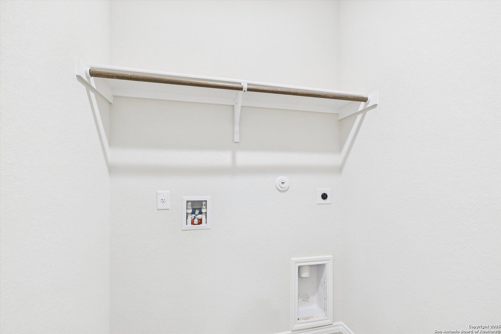 Modern laundry room with wooden hanging rod, utility sink, and built-in shelves in The Asheville K home, Bricewood, San Antonio