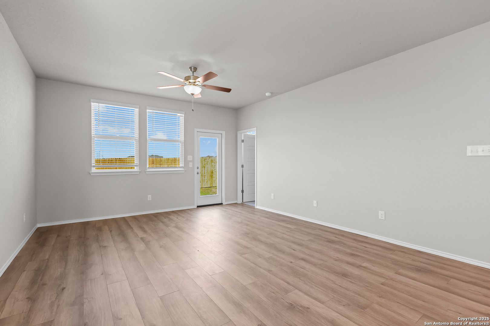 Bright living room with light gray walls, hardwood floors, ceiling fan, and French doors to patio in Davidson Homes The Colorado B, San Antonio