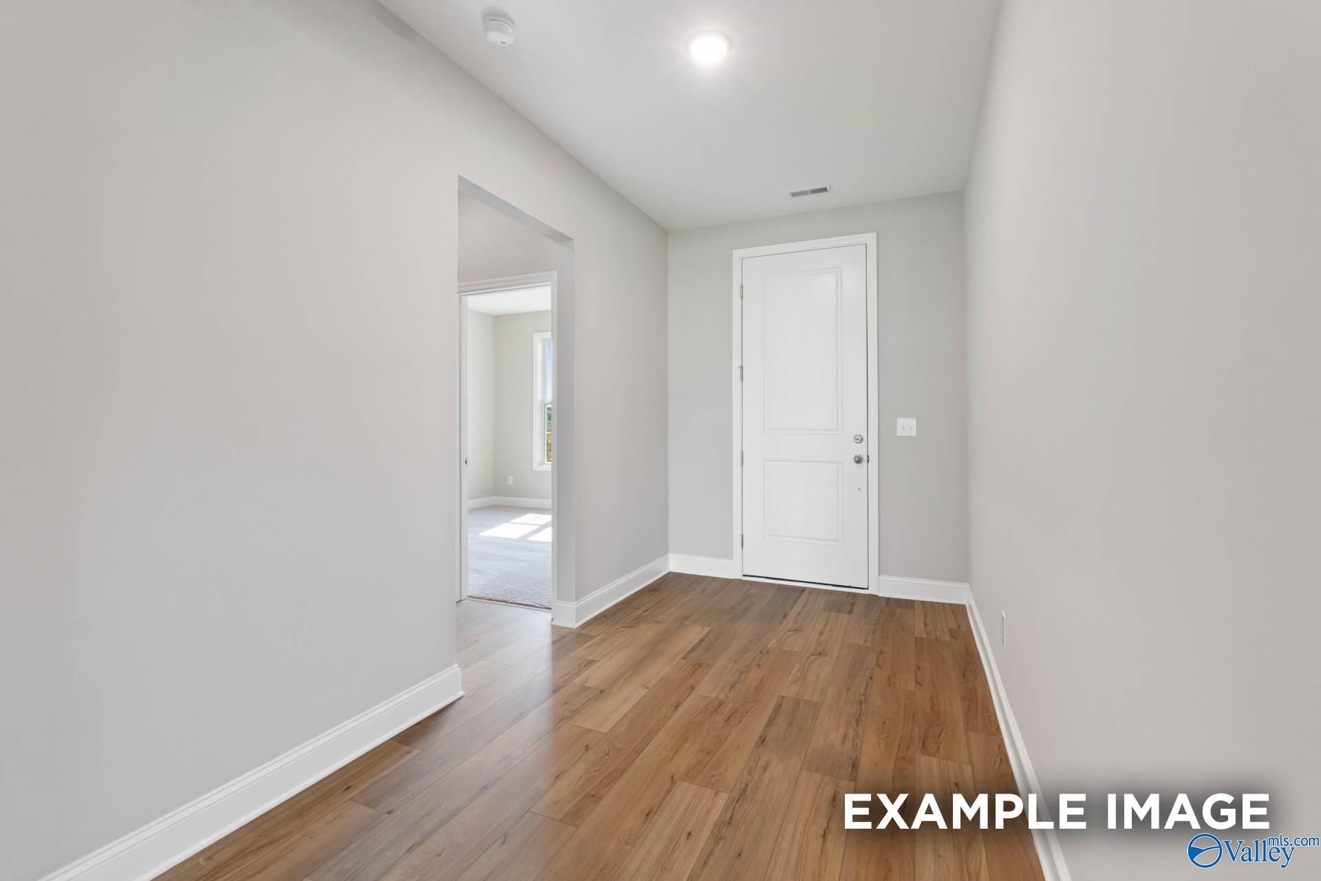 Modern hallway with light gray walls, hardwood floors, and open doorway in Davidson Homes Montgomery B, Hartselle, Alabama