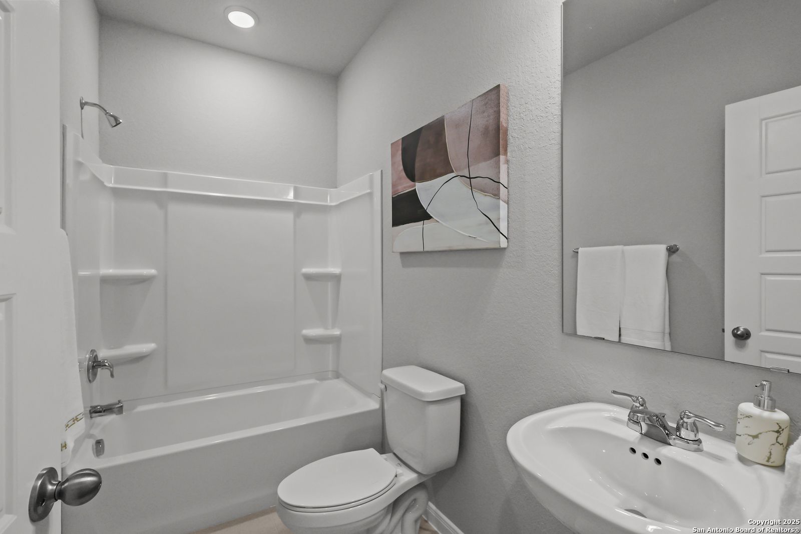 Modern guest bathroom with bathtub-shower combo, white subway tiles, vanity sink, and abstract wall art in Davidson Homes The Gillian C, San Antonio