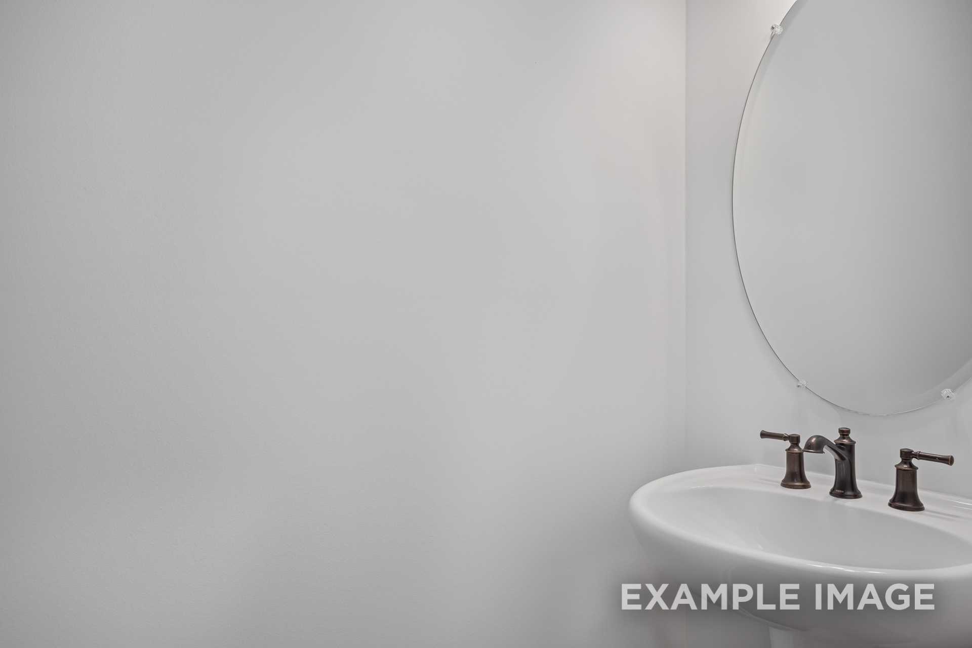 Modern bathroom vanity in The Grace C home with white sink, bronze faucets, and round mirror on gray wall