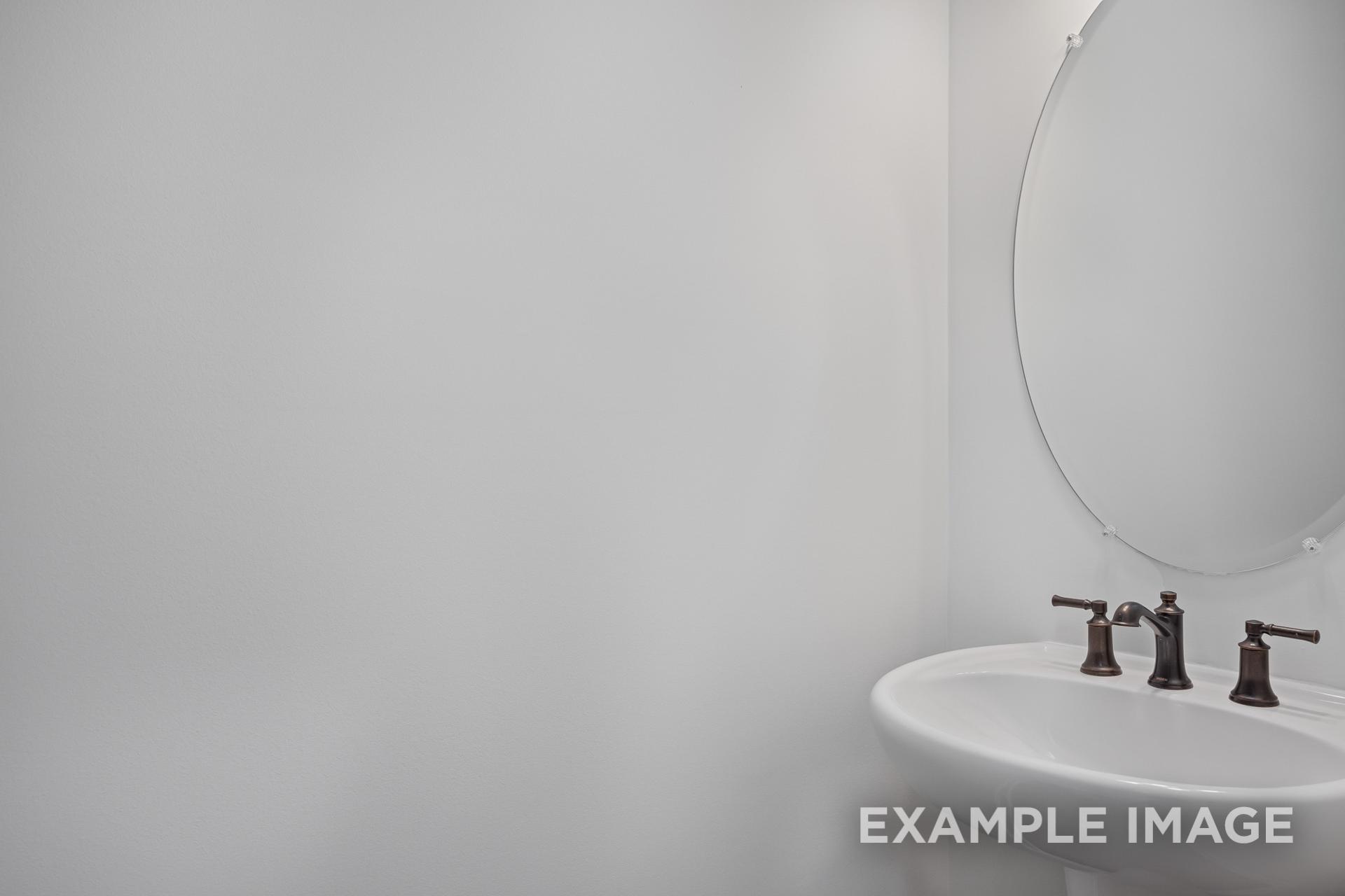 Modern bathroom vanity in The Grace C home with white sink, bronze faucets, and round mirror on gray wall