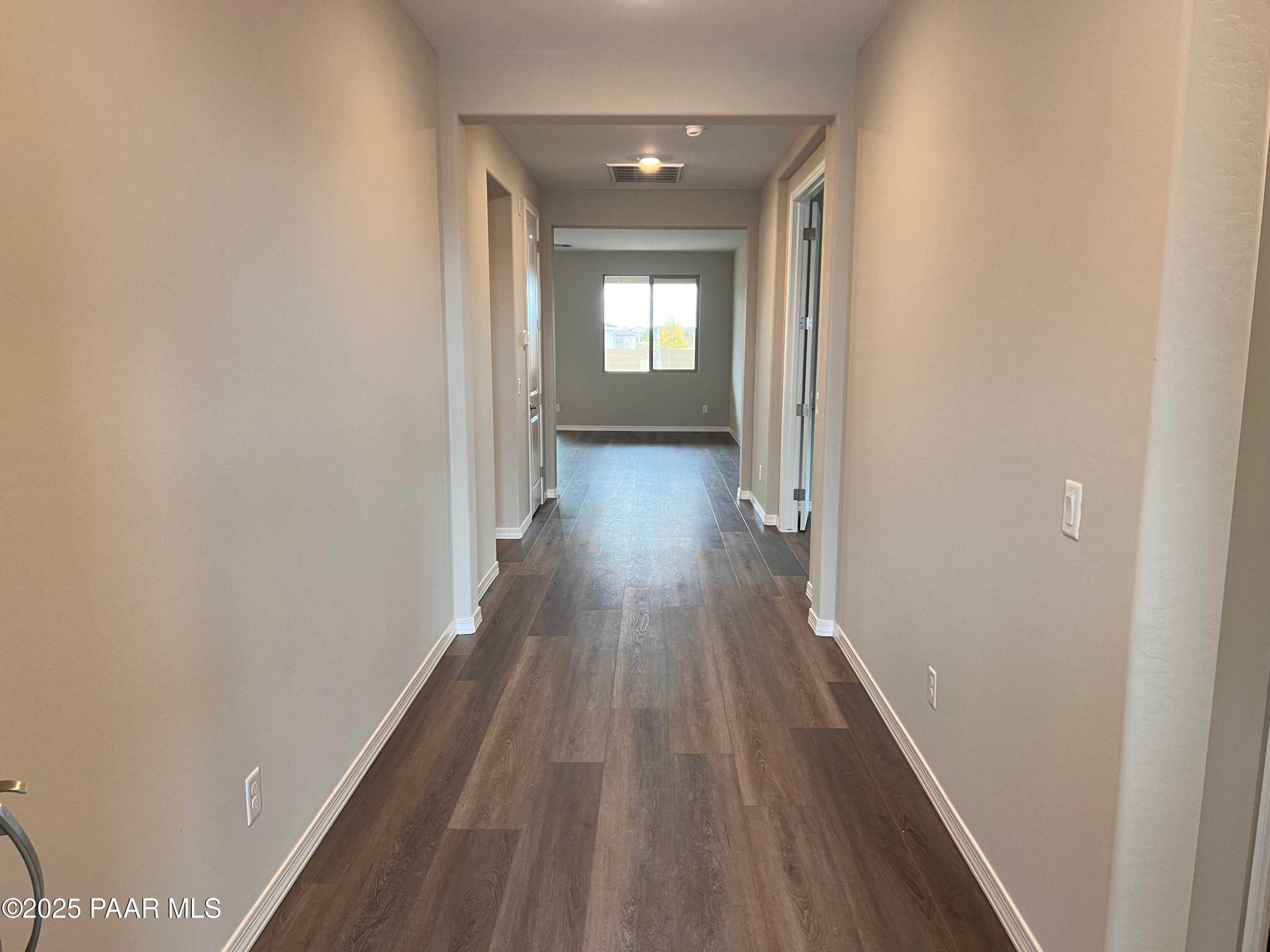 Spacious hallway with light wood floors, beige walls, side doors, and window view in Davidson Homes The Harmony A, Prescott Valley, AZ