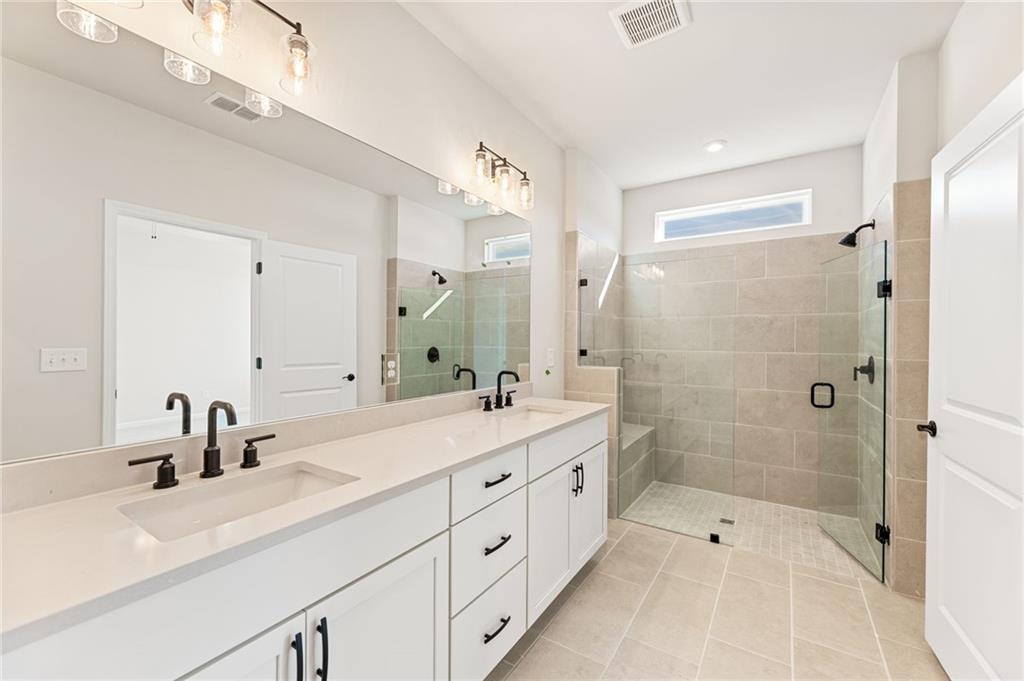 Elegant master bathroom with double vanity, frameless glass shower, and beige tile in Davidson Homes The Glenwood A, Loganville, GA