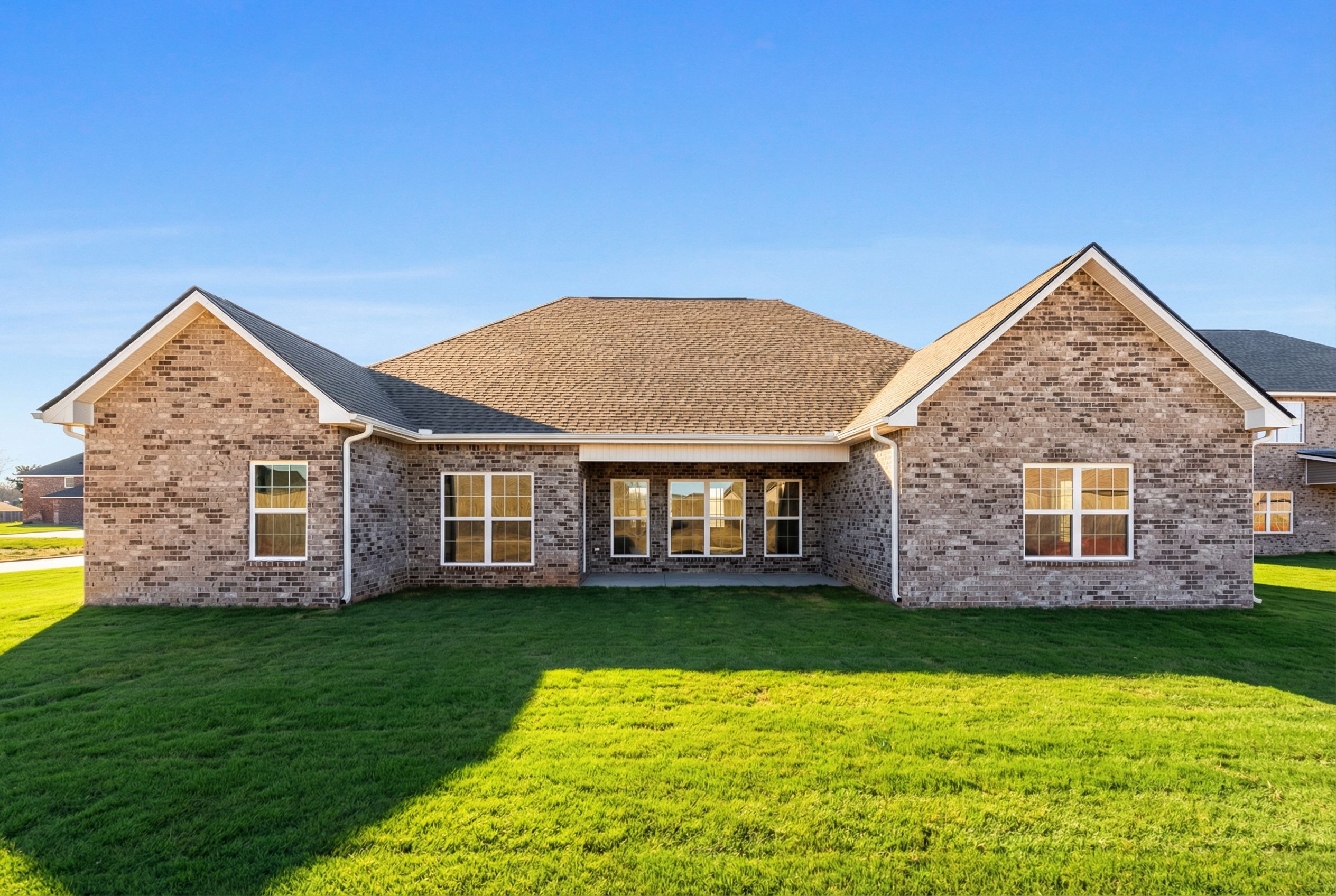 Rear elevation of Valencia single-story home with brick facade, hip roof, covered patio, large windows, and lush green lawn
