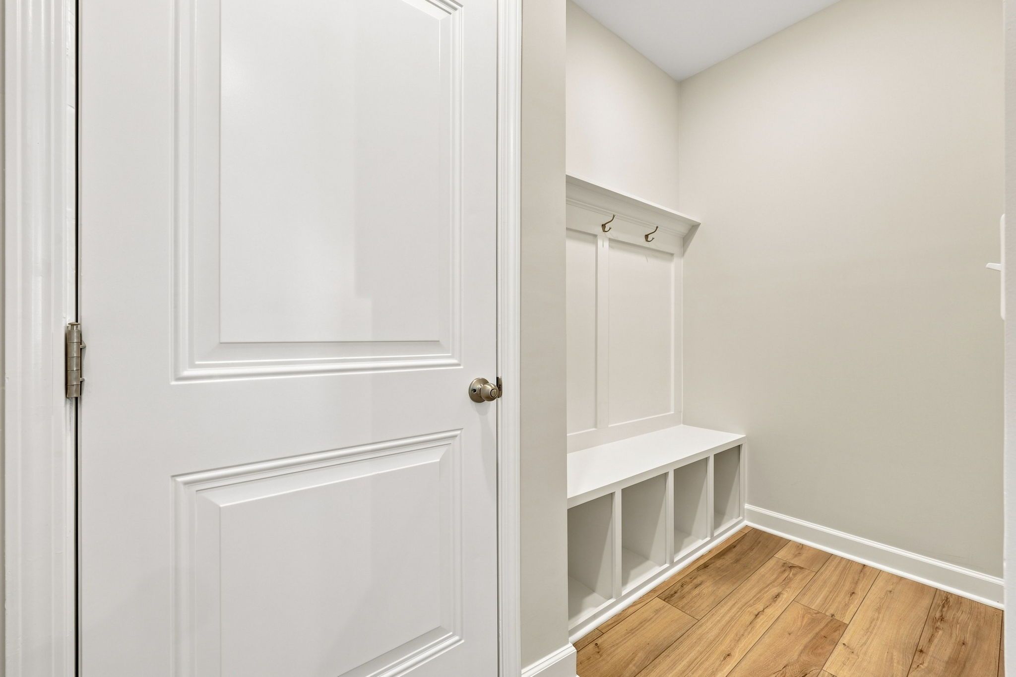 Mudroom drop zone with white built-in bench, storage cubbies, and coat hooks in The Jordan A home design.