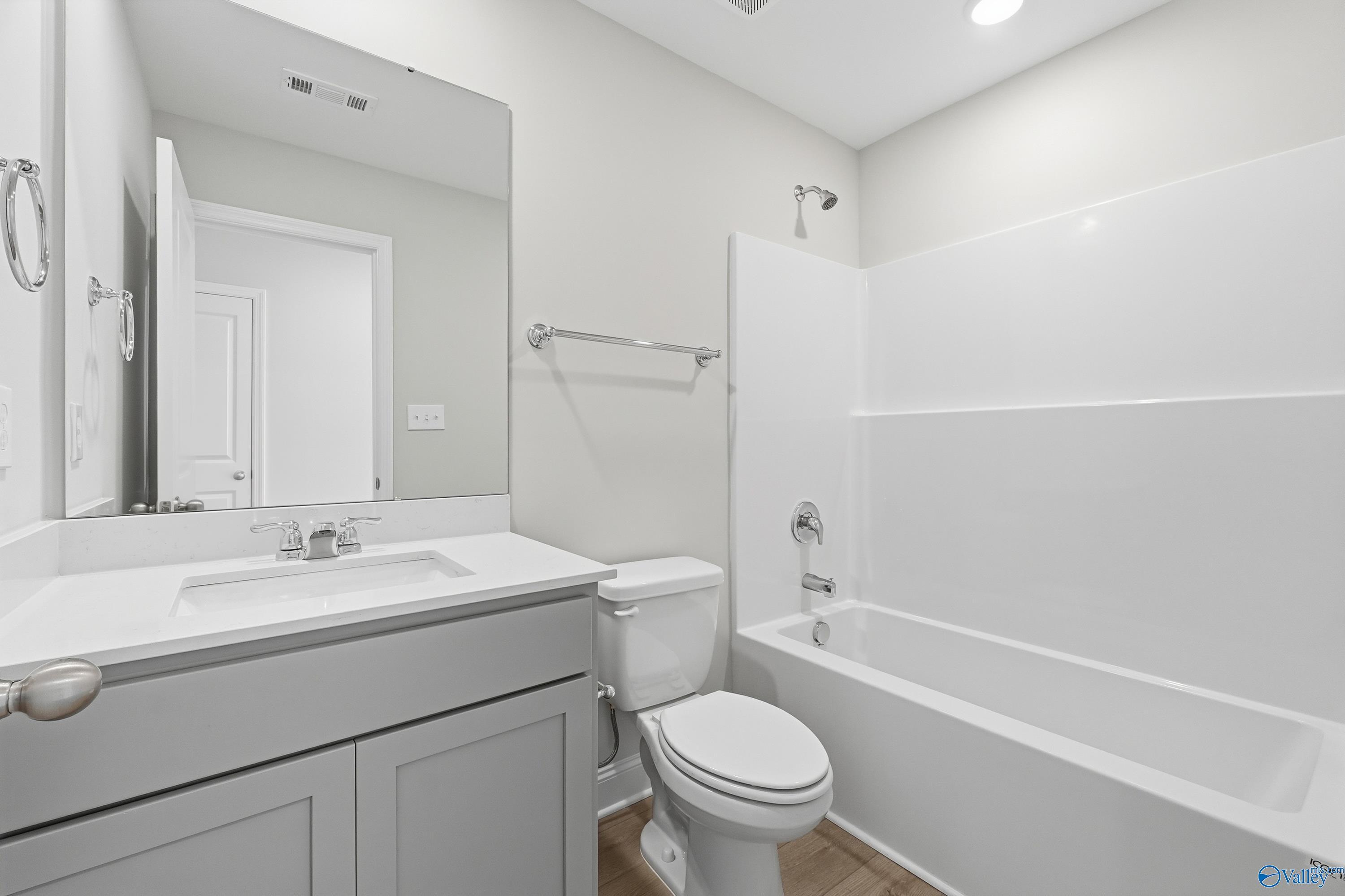 Bright bathroom with white subway tile shower, soaking tub, gray vanity, and toilet in Davidson Homes The Butler, New Market, Alabama