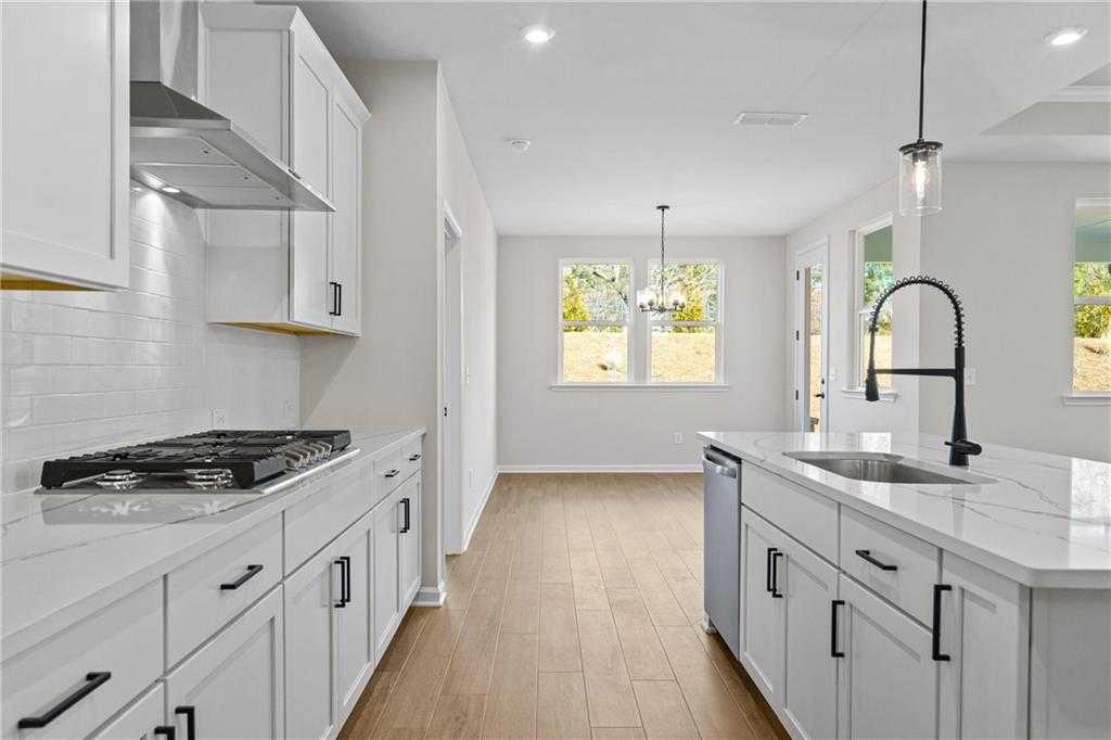 Modern white kitchen with quartz island, gas cooktop, stainless appliances in open-concept The Edison A by Davidson Homes, Loganville, GA