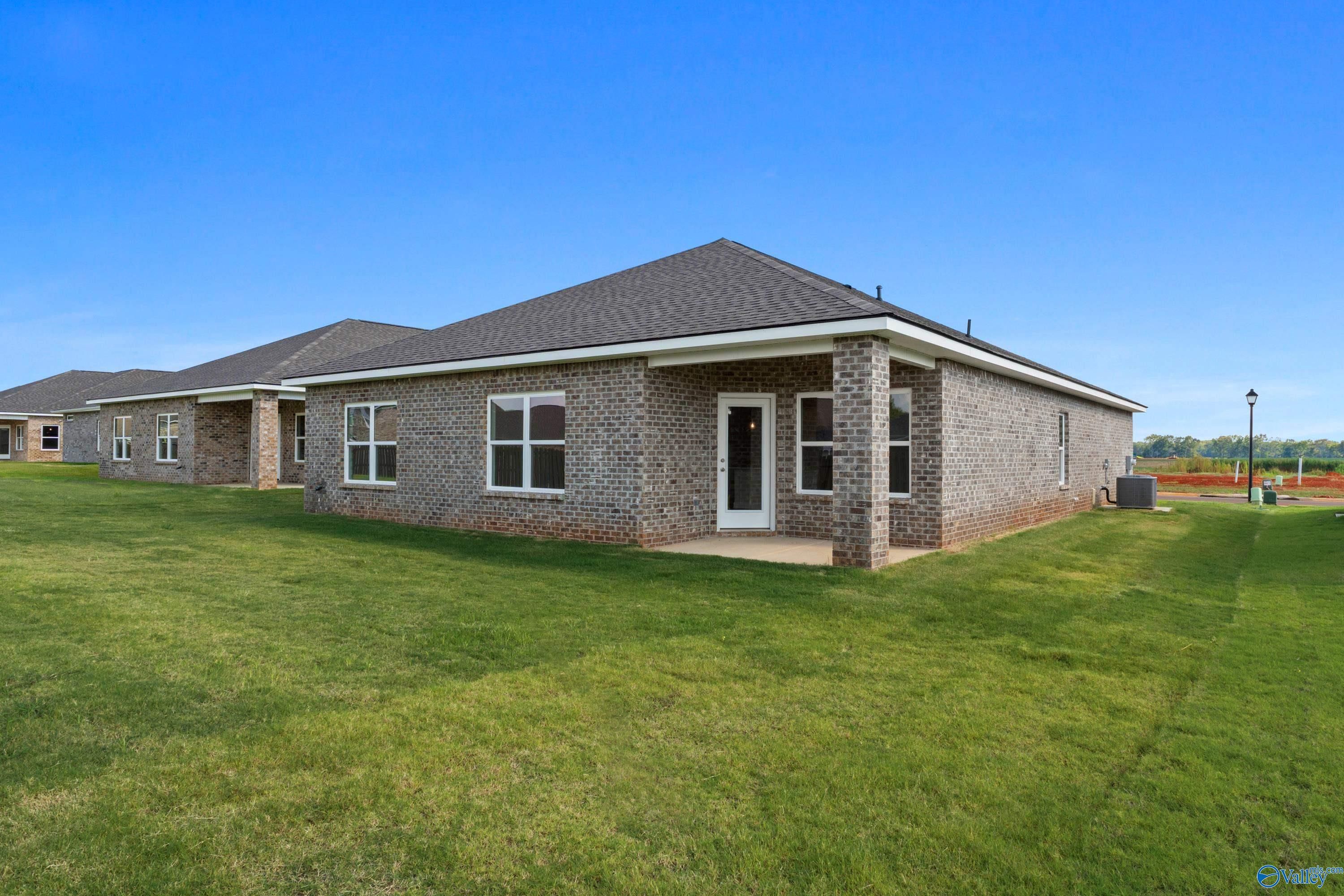 Side view of brick ranch-style Daphne home by Davidson Homes in Clearview, Hazel Green, Alabama, with windows, covered entry, lush green lawn, blue sky