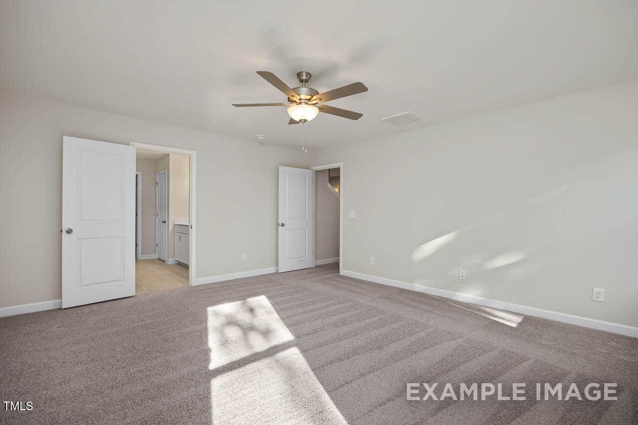 Bright bedroom with ceiling fan, beige walls, carpet floor, and open door to bathroom in Davidson Homes The Hickory II B, Lillington, NC