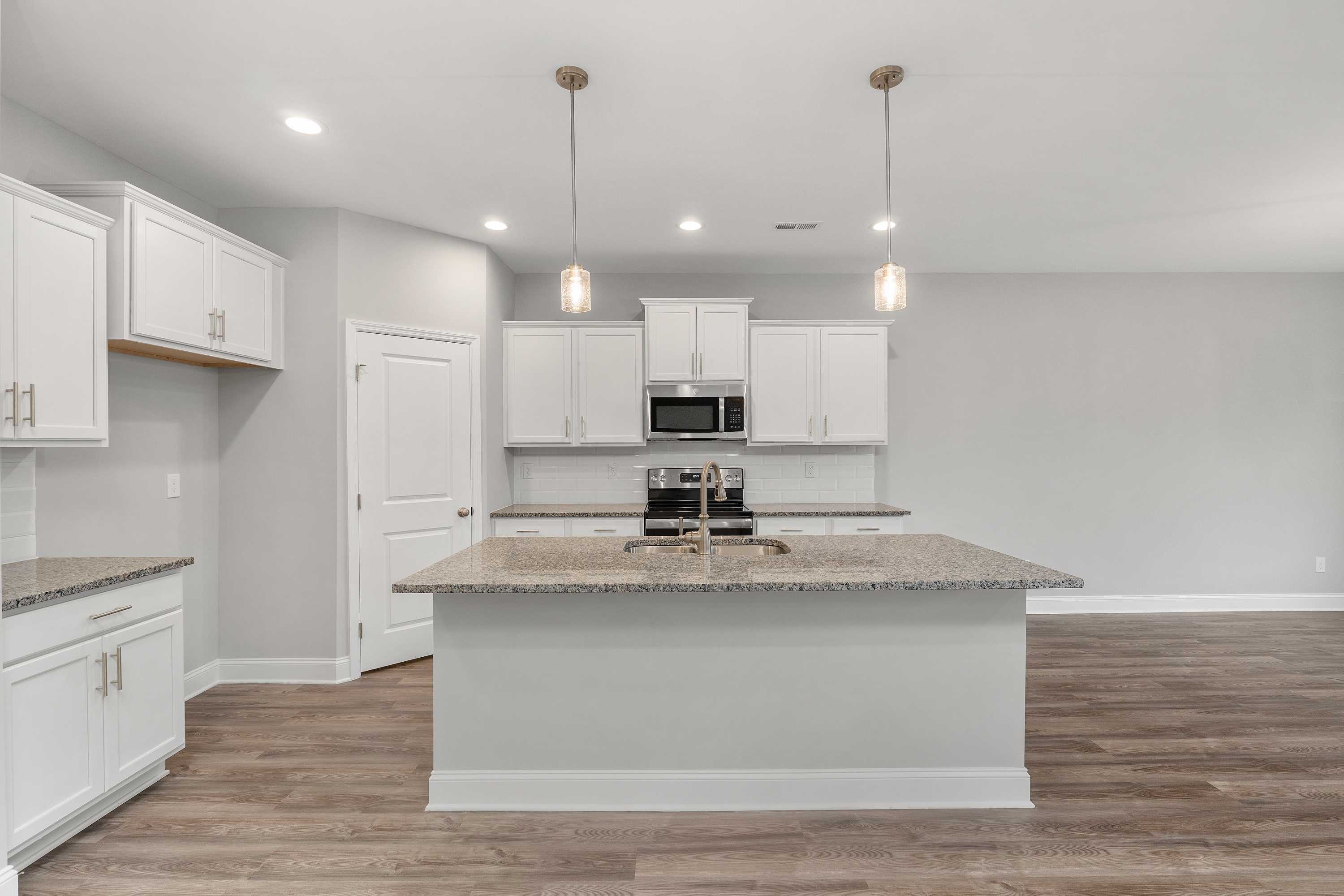 Modern kitchen in The Aiken by Davidson Homes featuring white cabinetry, granite island with sink, stainless appliances, pendant lights, hardwood floors
