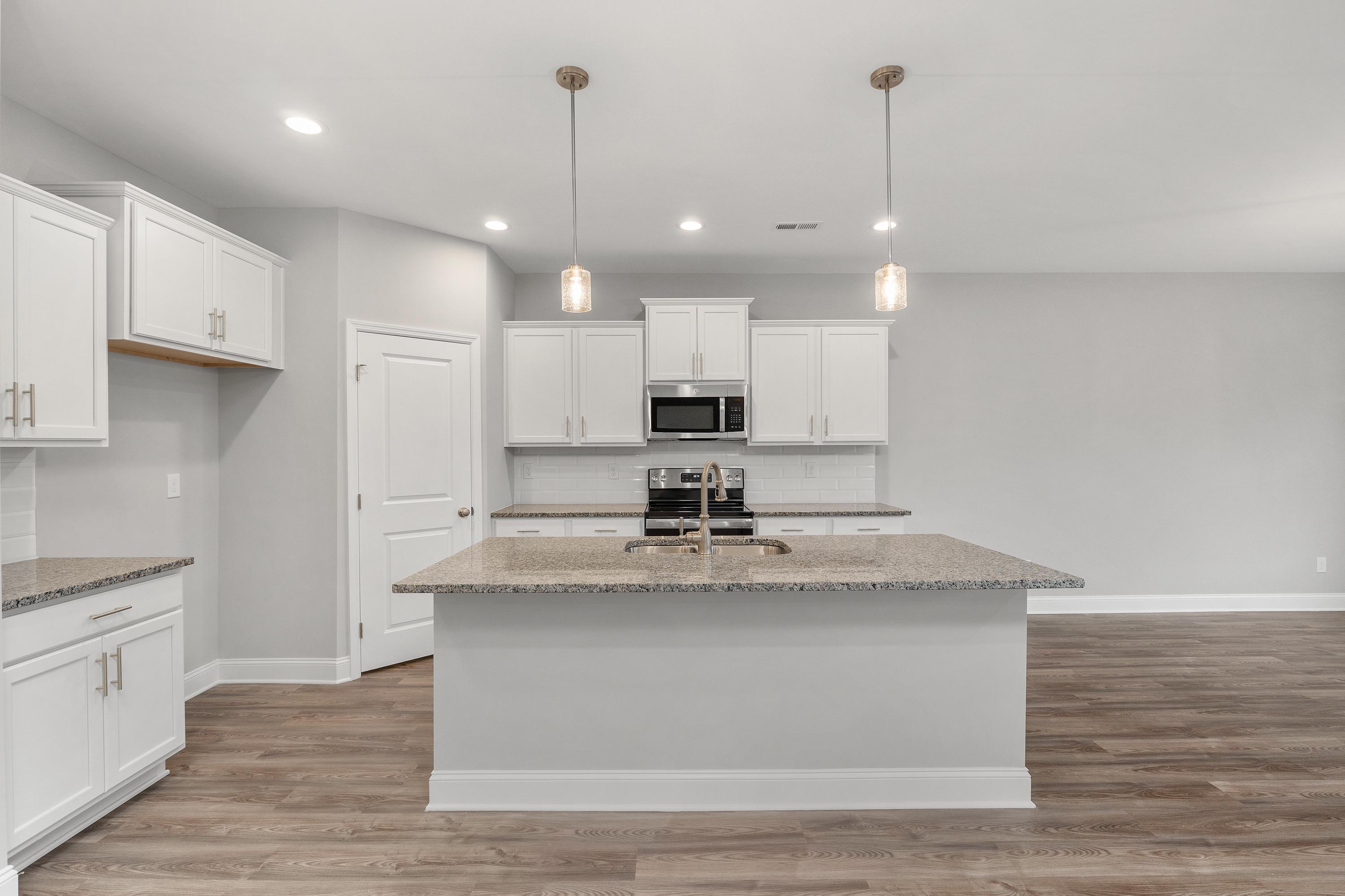 Modern kitchen in The Aiken by Davidson Homes featuring white cabinetry, granite island with sink, stainless appliances, pendant lights, hardwood floors