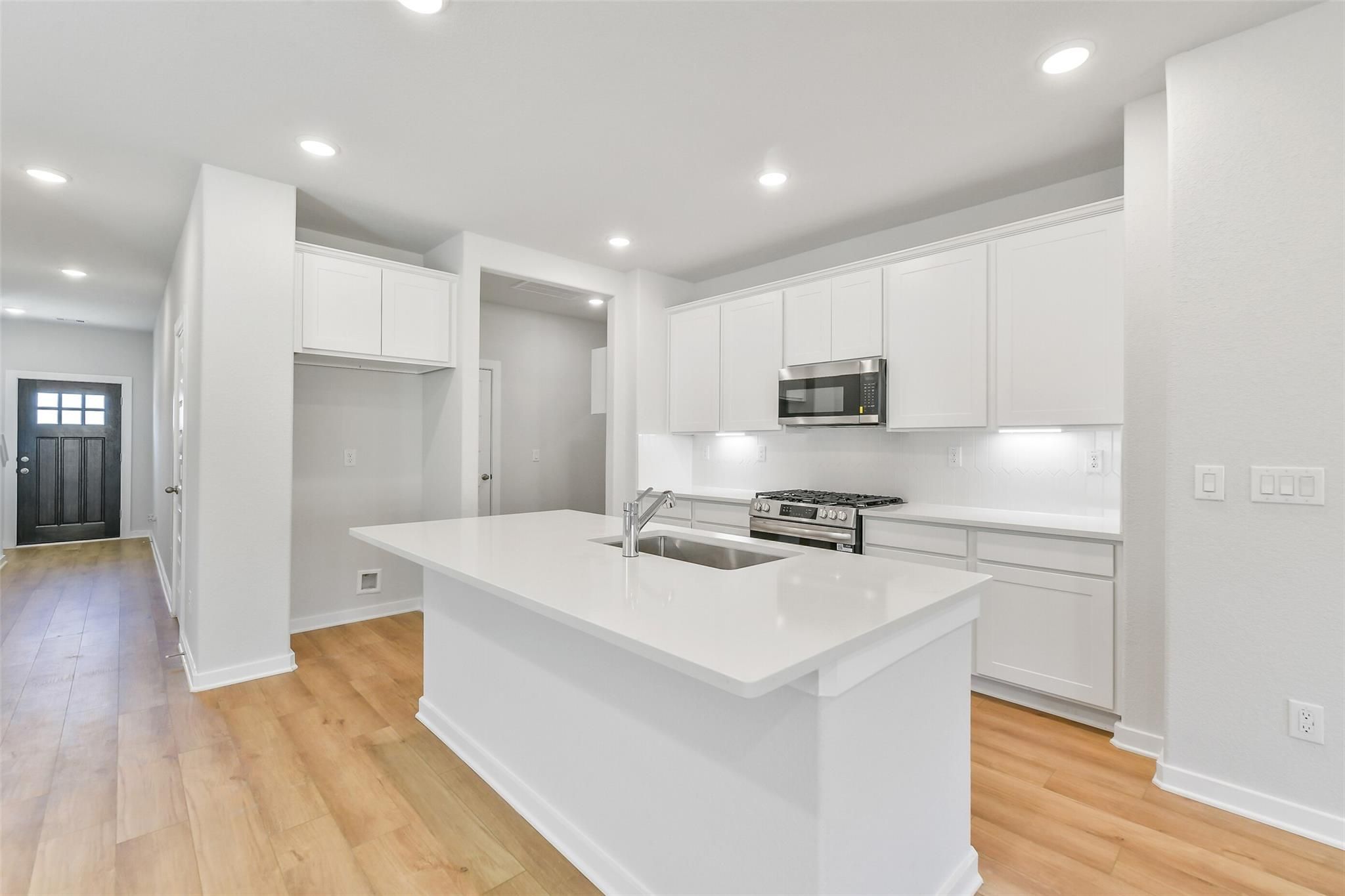 Modern white kitchen with large island, stainless appliances, and hardwood floors in Davidson Homes The Blanco E, Magnolia, Texas