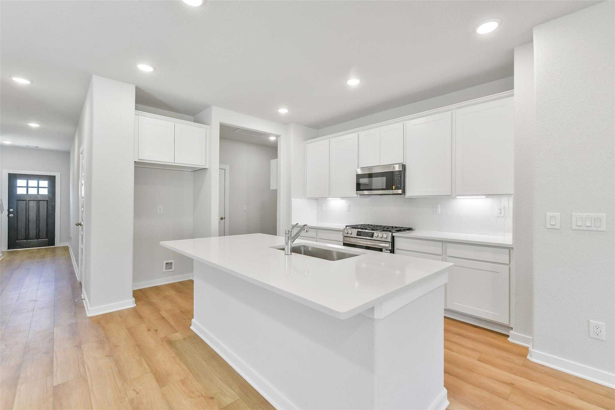 Modern white kitchen with large island, stainless appliances, and hardwood floors in Davidson Homes The Blanco E, Magnolia, Texas