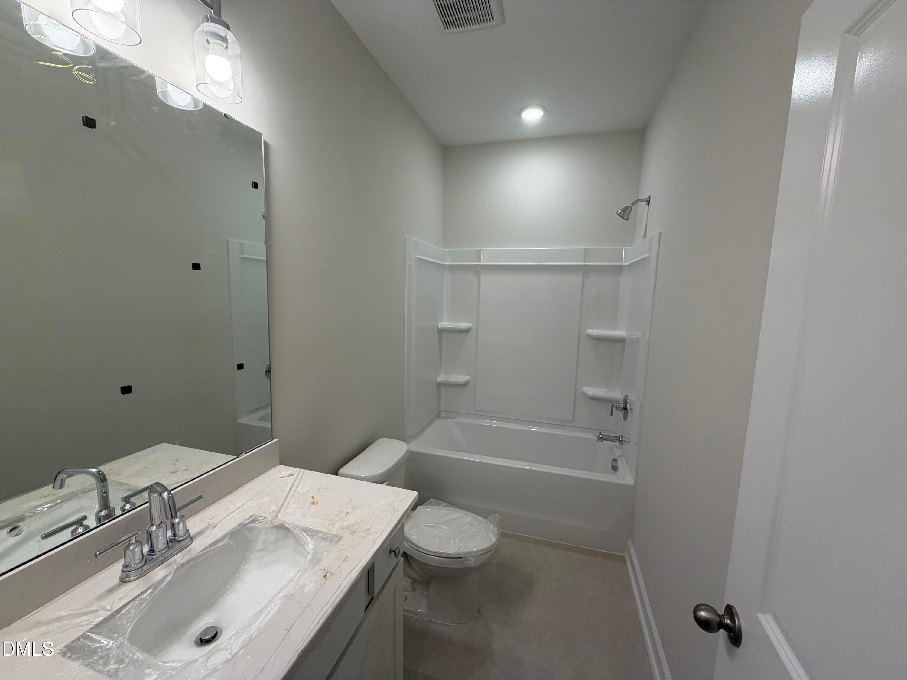 Modern guest bathroom with white tub-shower combo, single vanity sink, large mirror, and neutral walls in Davidson Homes The Daphne C, Lillington, NC