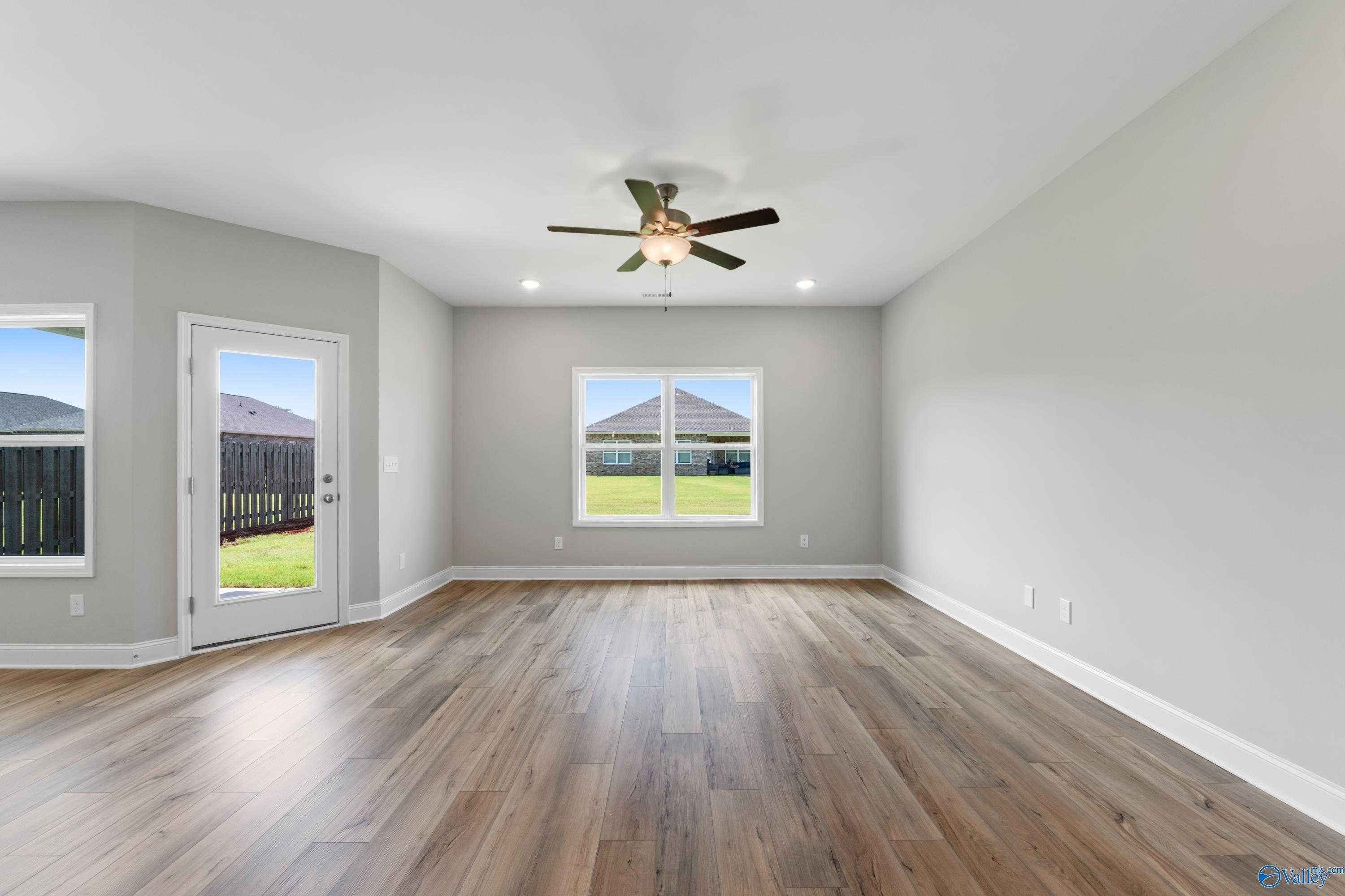 Bright family room with gray walls, hardwood floors, ceiling fan, sliding door to backyard, and yard views in Davidson Homes The Daphne C, Athens, Alabama