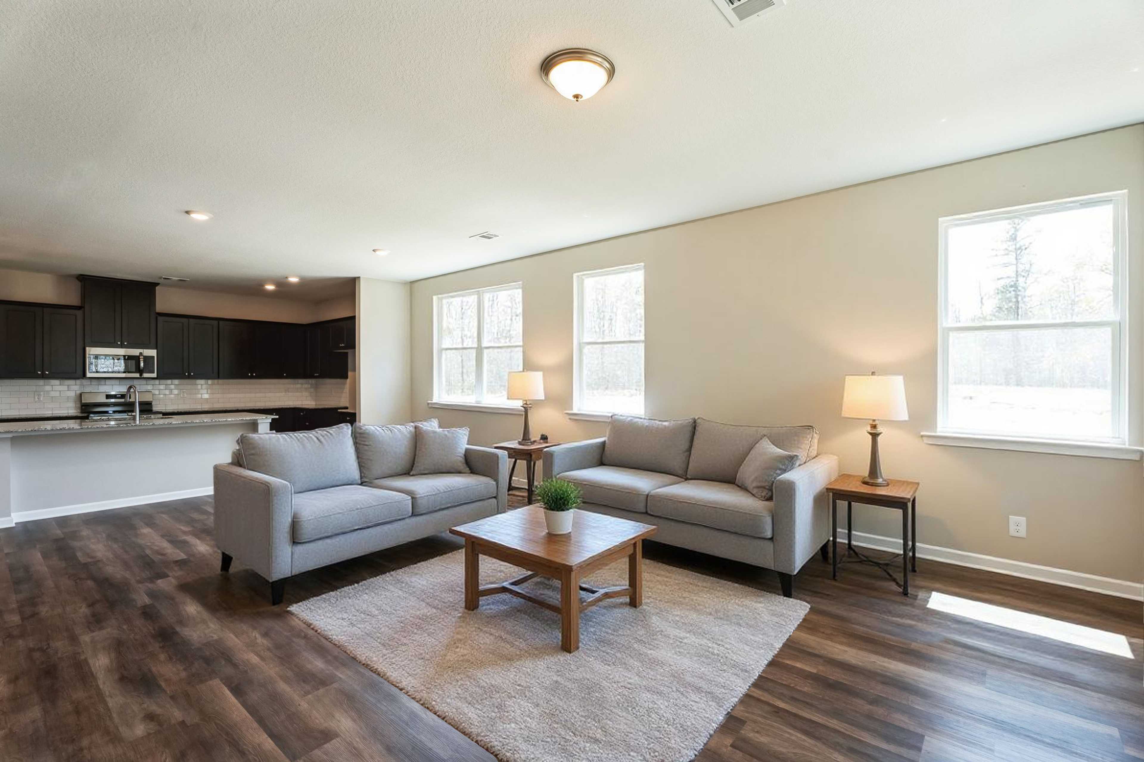 Open-concept living room in Heatherbrook by Evermore Homes featuring gray sofas, hardwood floors, and modern kitchen in Phenix City Alabama