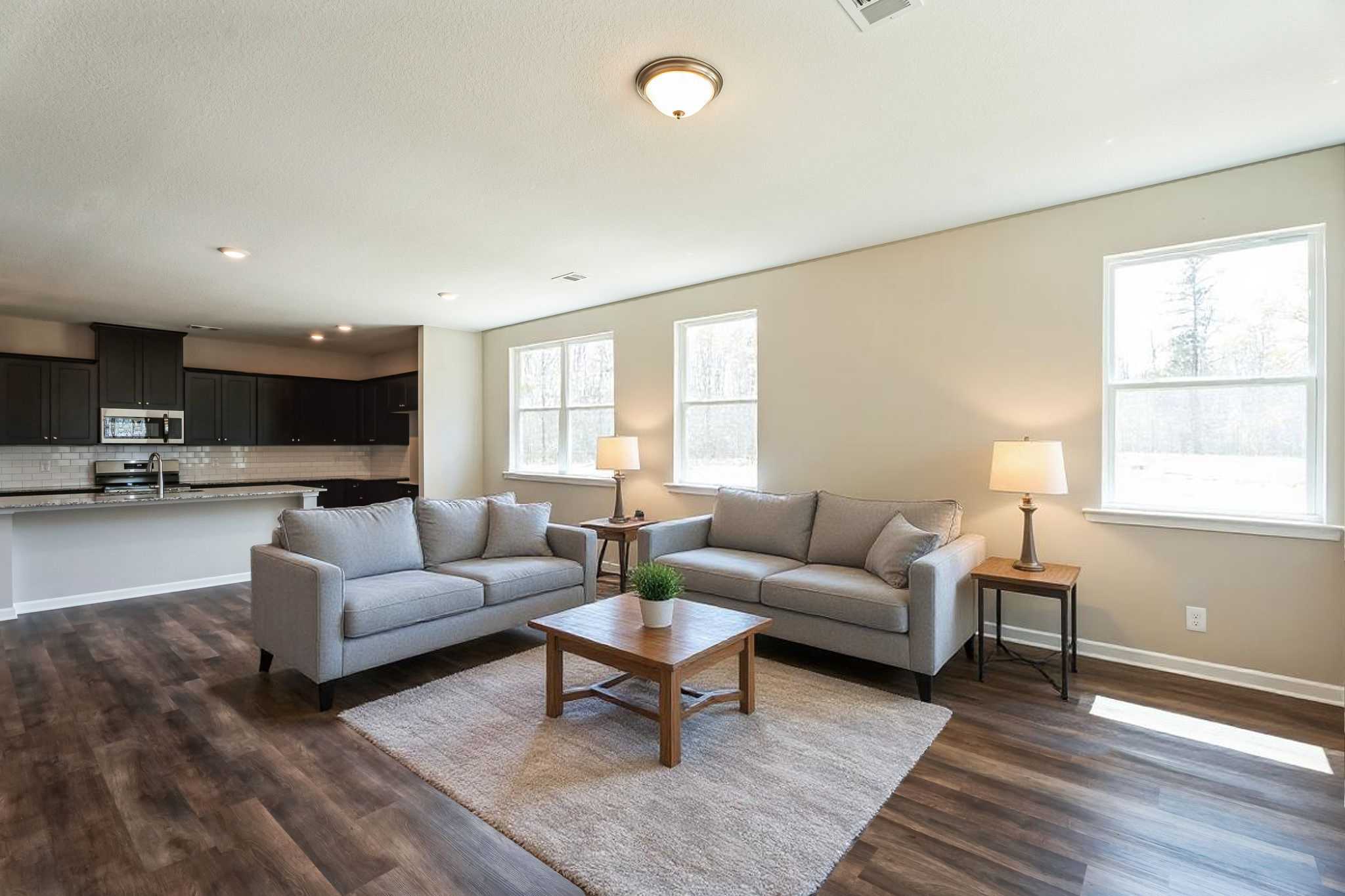 Open-concept living room in Heatherbrook by Evermore Homes featuring gray sofas, hardwood floors, and modern kitchen in Phenix City Alabama