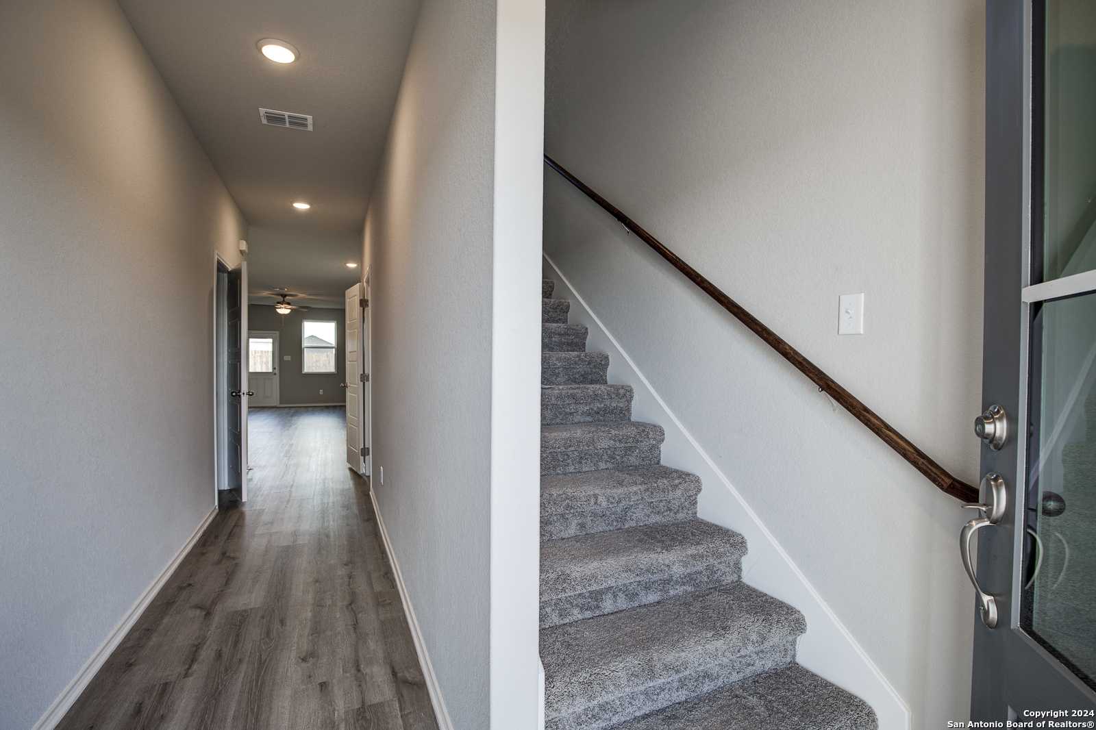 Bright hallway with laminate wood flooring and recessed lights adjacent to carpeted staircase in Davidson Homes The Blanco C, San Antonio