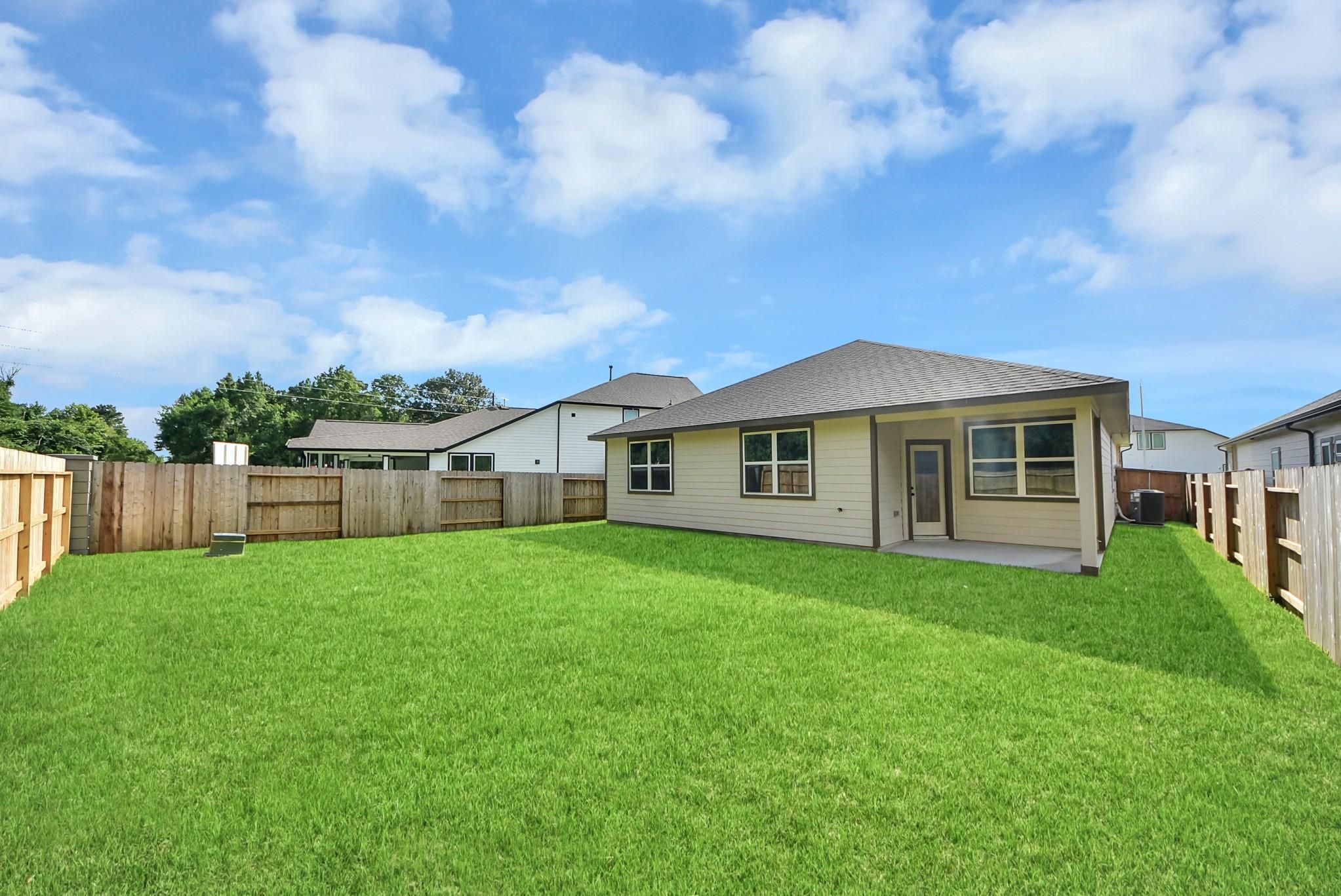 Private backyard with green lawn and covered patio at The Daphne F floor plan in Sundance Cove, Crosby, Texas.