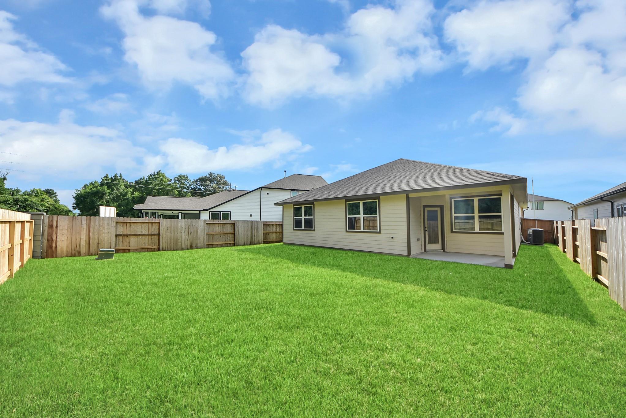 Private backyard with green lawn and covered patio at The Daphne F floor plan in Sundance Cove, Crosby, Texas.