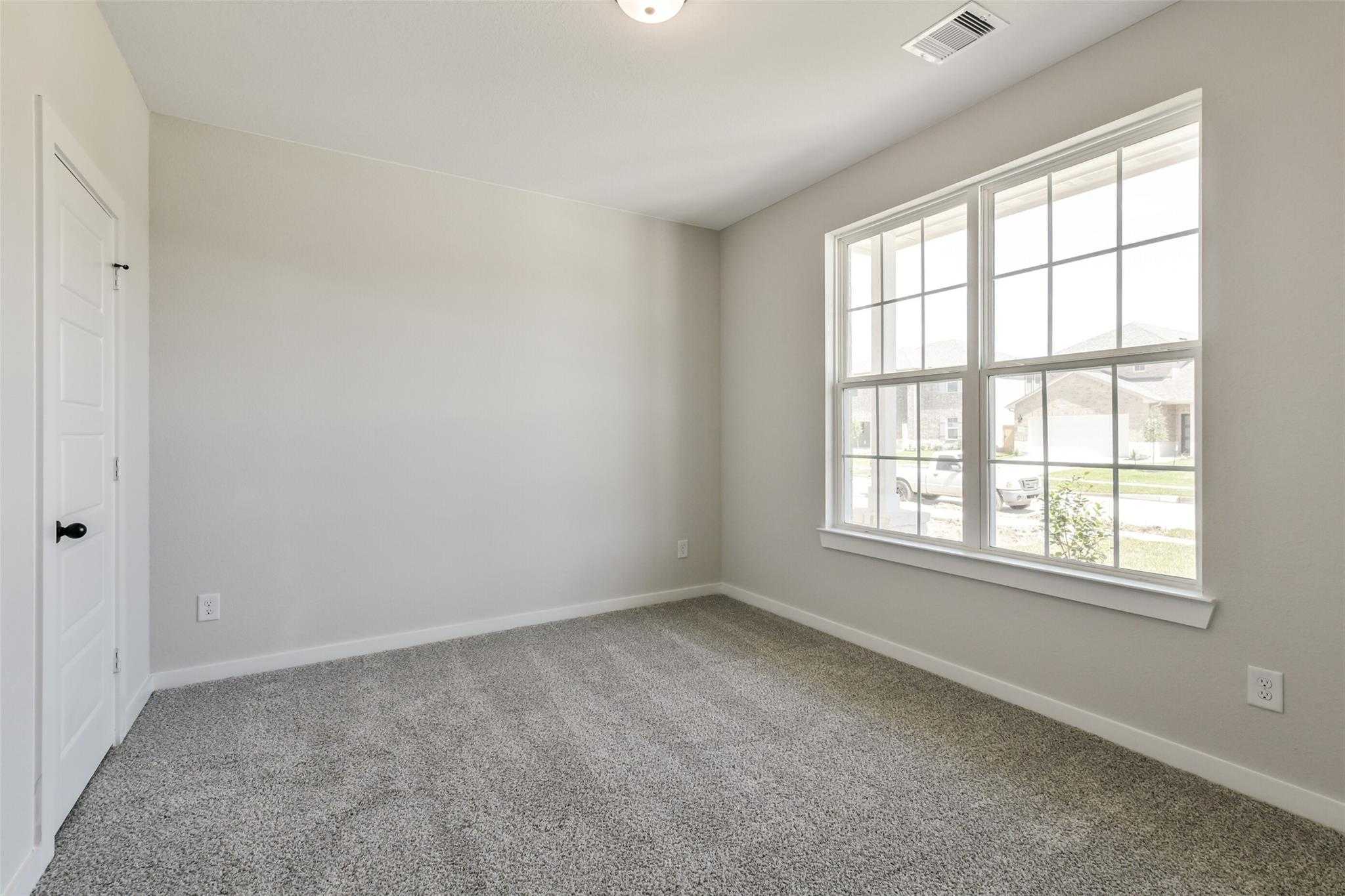 Bright secondary bedroom with beige walls, gray carpet, and large window view in Davidson Homes The Daphne H, Sundance Cove, Crosby, Texas