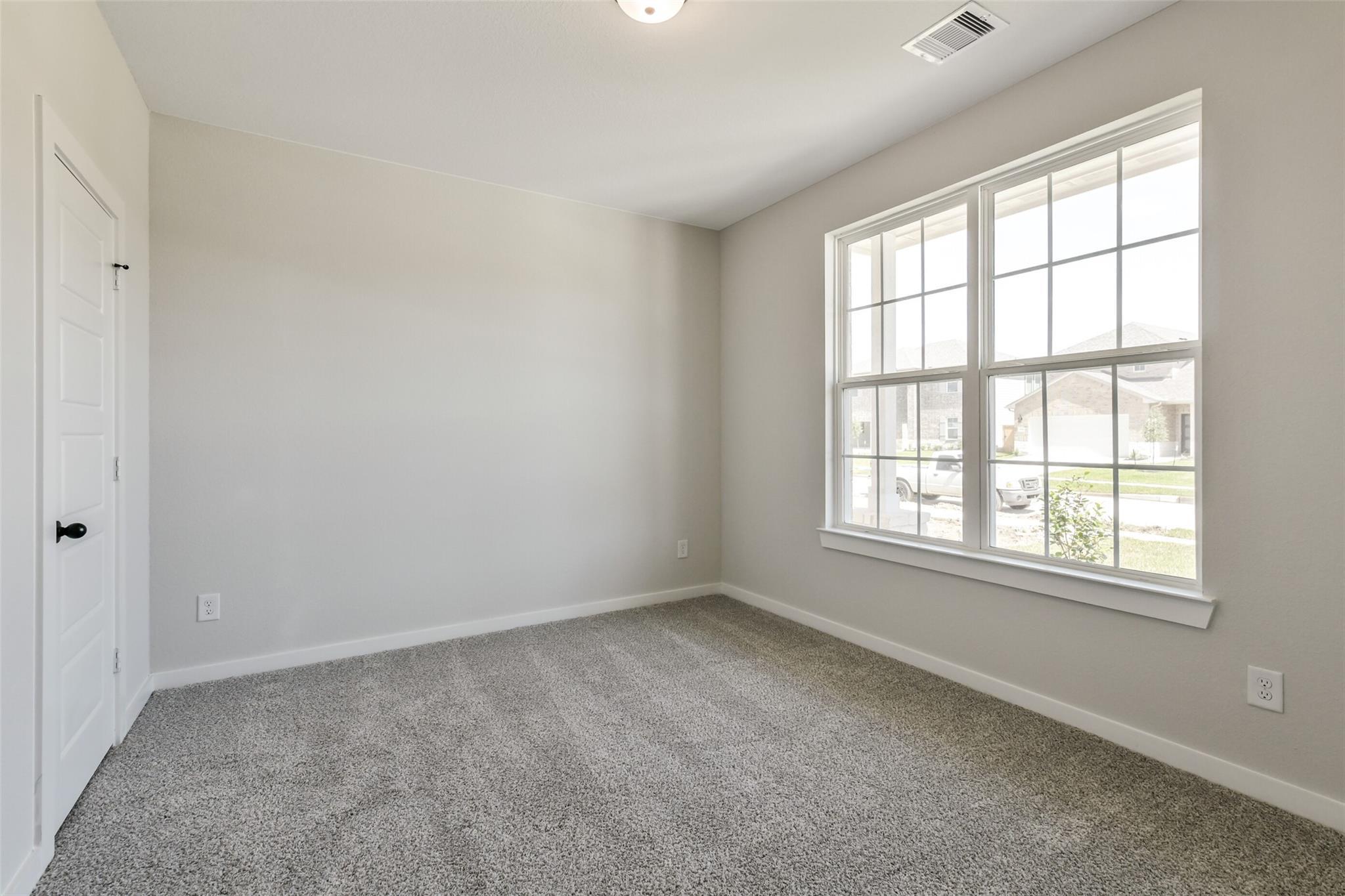 Bright secondary bedroom with beige walls, gray carpet, and large window view in Davidson Homes The Daphne H, Sundance Cove, Crosby, Texas
