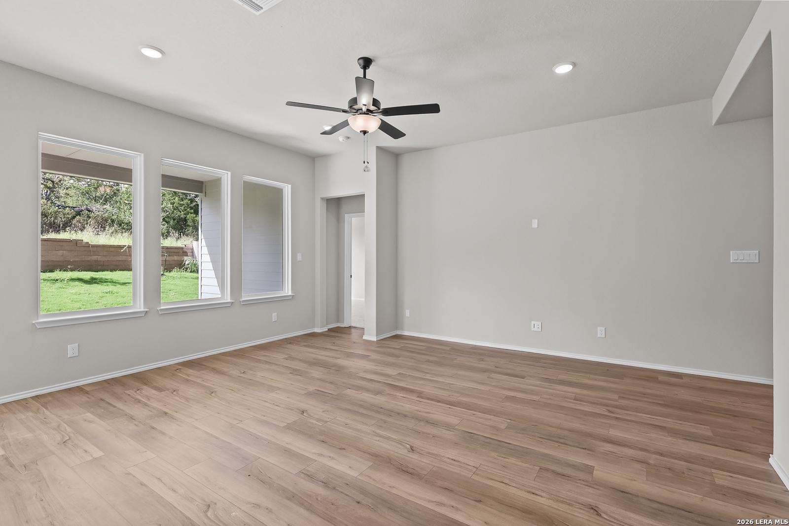 Bright open-concept living room with wood-look tile flooring and backyard windows in The Sequoia C by Davidson Homes, San Antonio