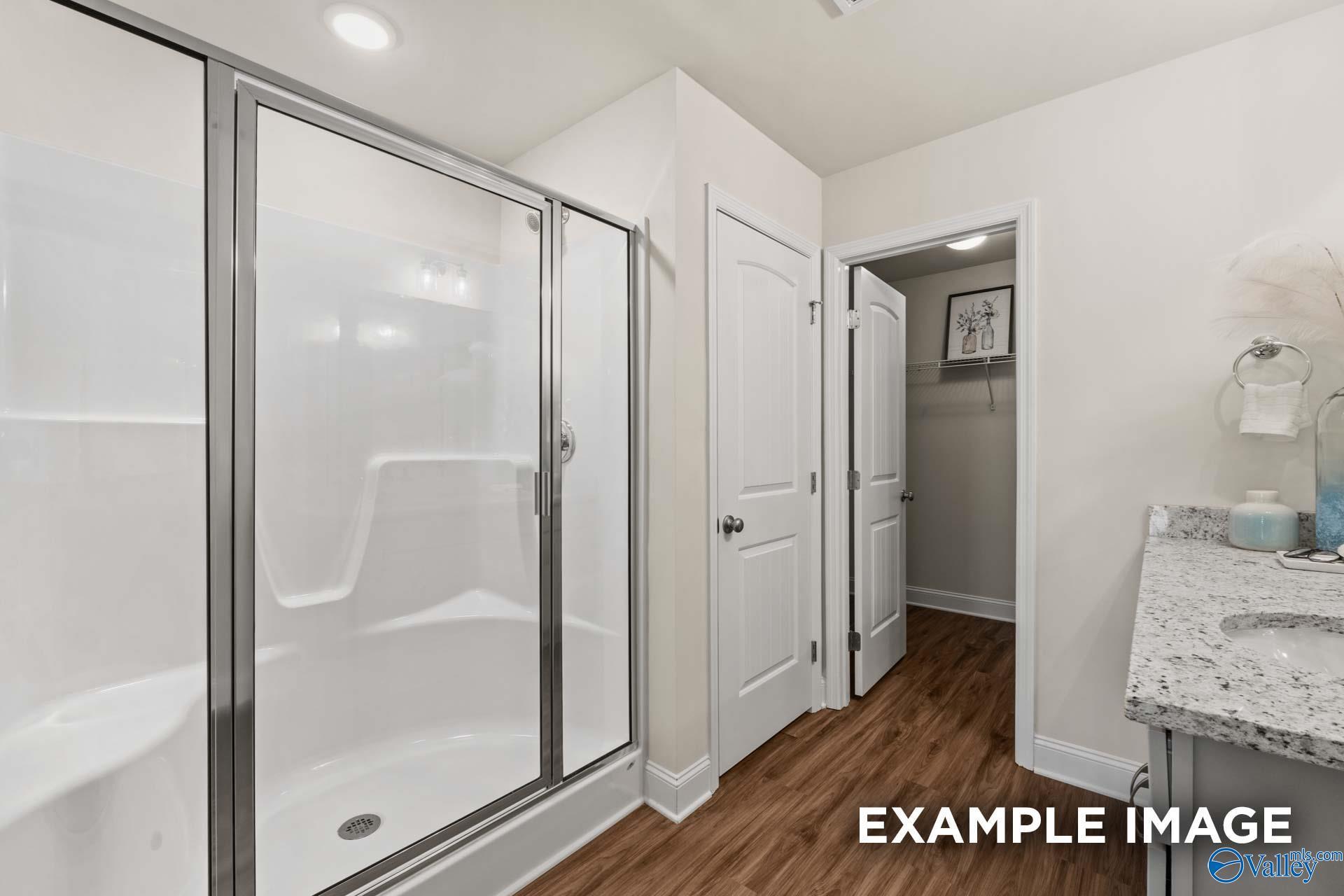 Modern master bathroom featuring frameless glass shower, granite vanity, and hardwood floors in Davidson Homes The Franklin C, New Market, Alabama