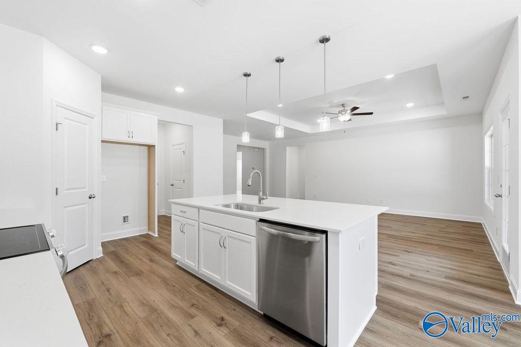 Modern open-concept kitchen with white island, stainless dishwasher, and hardwood floors in The Montgomery 3-bedroom home, Hartselle, Alabama