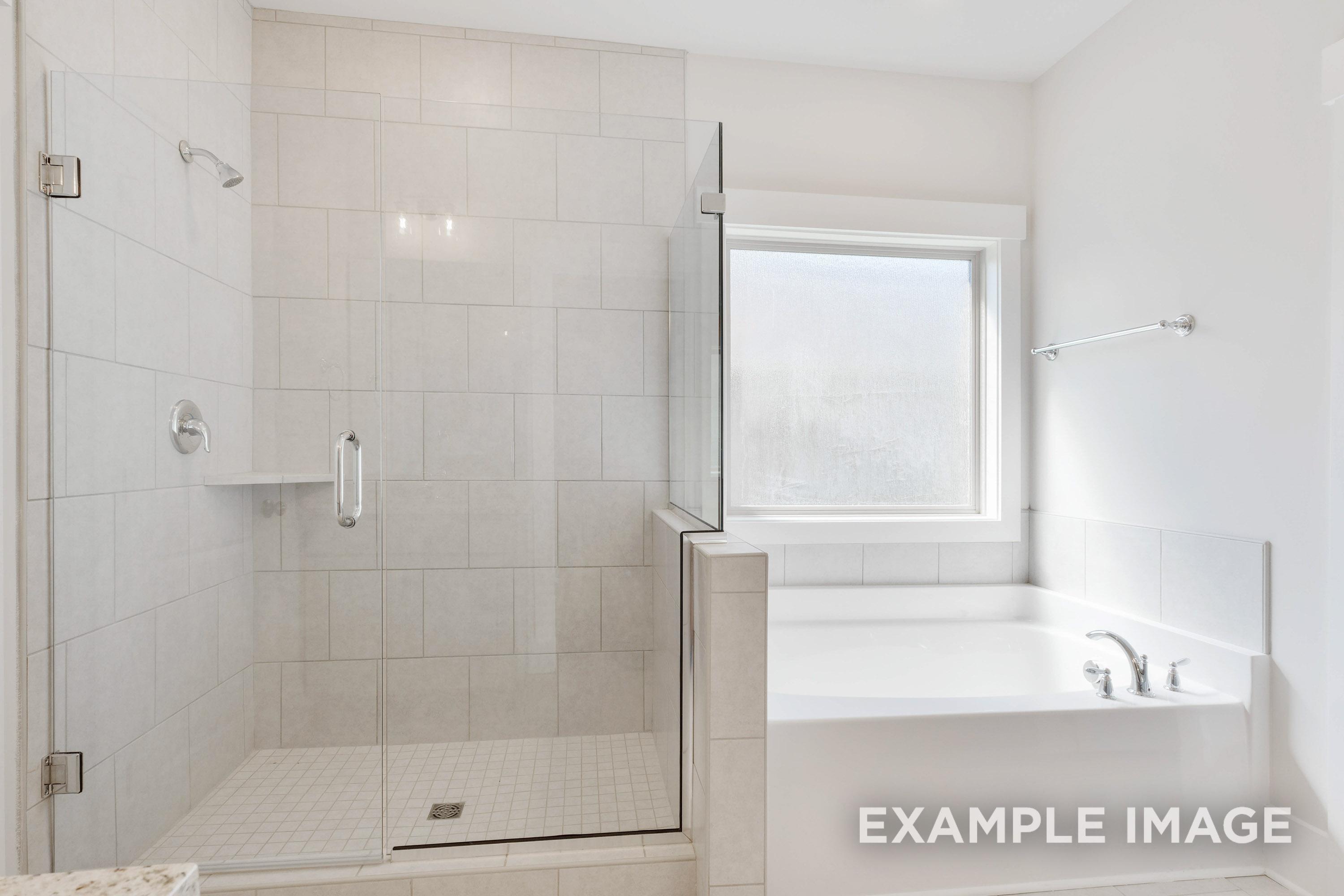 Master bathroom in The Richmond D featuring a walk-in glass shower and deep soaking tub with neutral tile finishes.