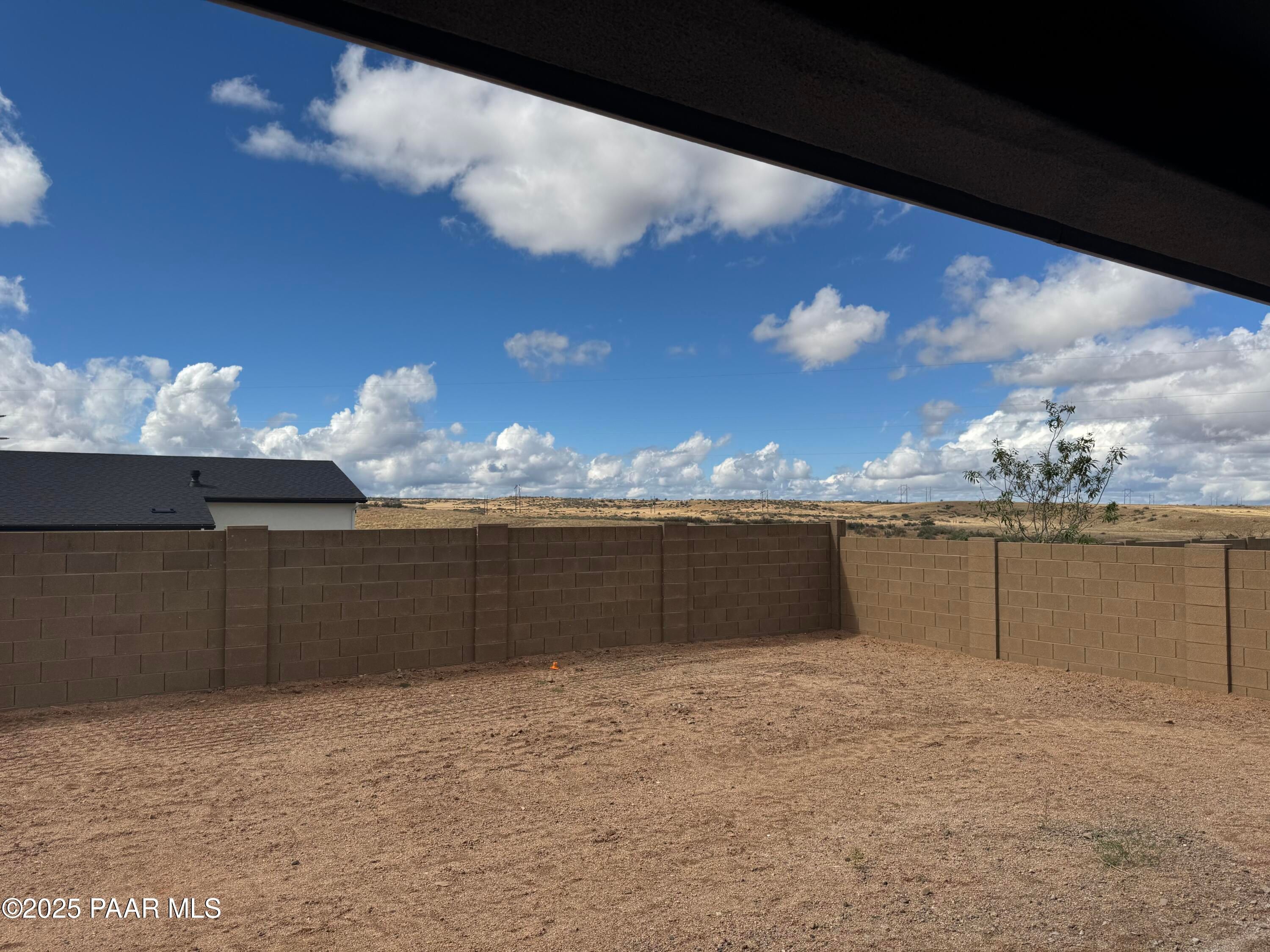Covered back patio overlooking spacious sandy backyard with block fence and desert landscape under blue sky in Westwood, Prescott, Arizona