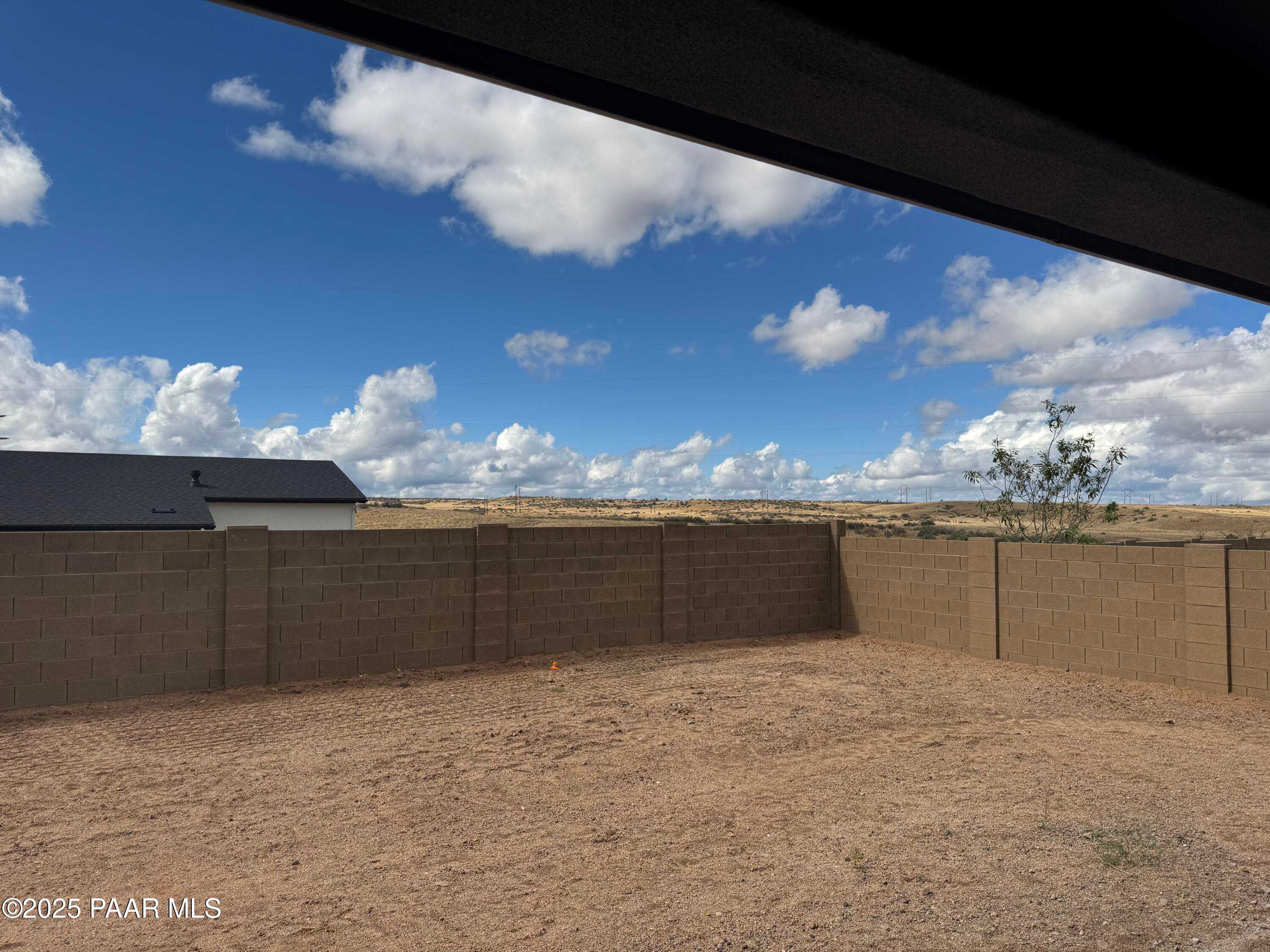 Covered back patio overlooking spacious sandy backyard with block fence and desert landscape under blue sky in Westwood, Prescott, Arizona