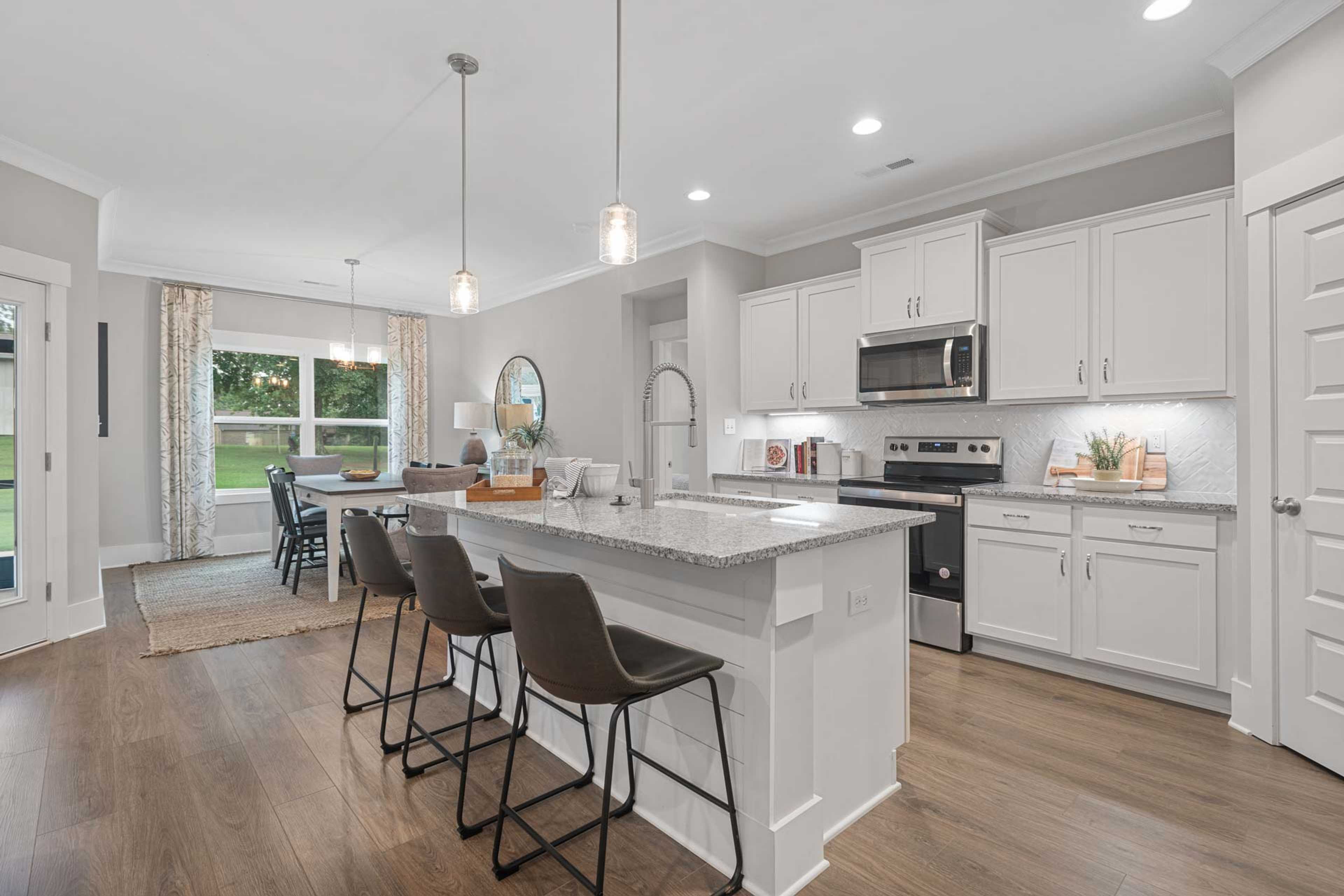 Open-concept kitchen at Monteagle Cove in Owens Cross Roads AL with white cabinets, granite island, stainless appliances, hardwood floors