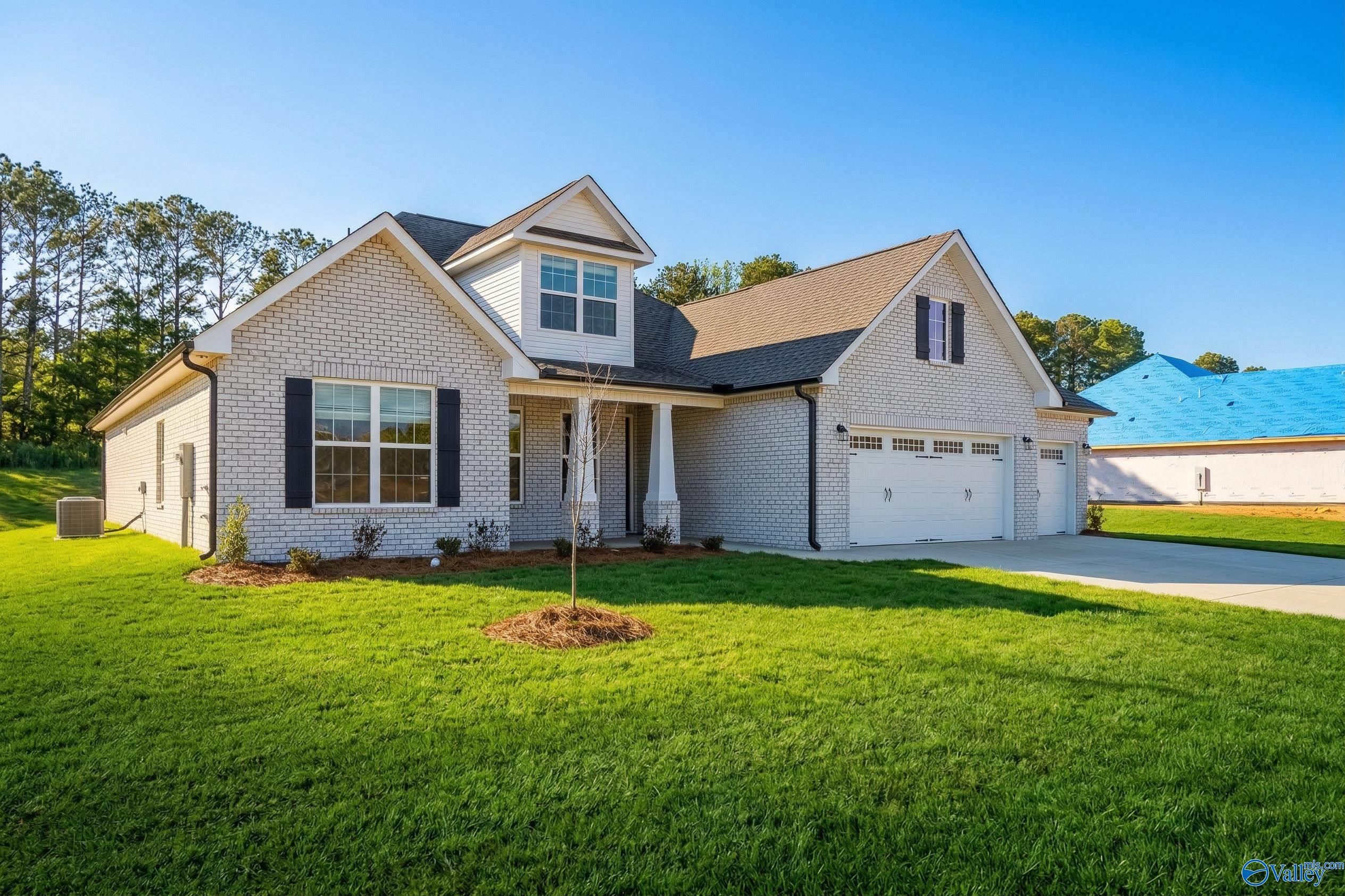 Charming 1.5-story white brick home with 3-car garage, front porch, and lush green yard in Cain Park, Hartselle, Alabama - Davidson Homes The Rockford