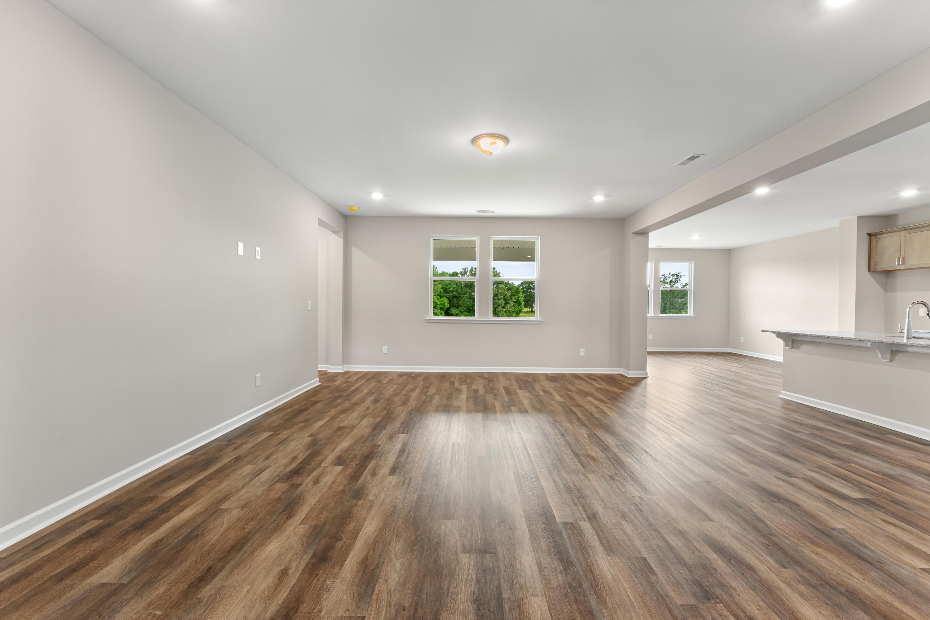 Spacious open-concept living room in The Haven E with hardwood floors, gray walls, large windows, and modern kitchen adjacent