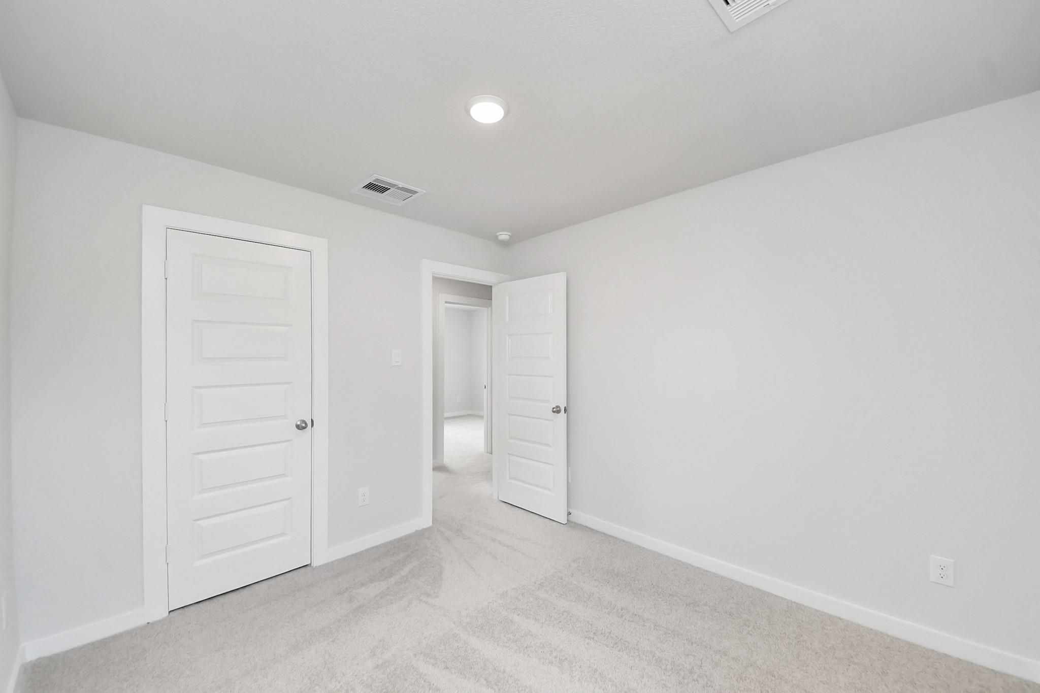 Bright, carpeted bedroom with white walls and interior doors in The Blanco E floor plan at Caney Creek Place, Conroe.