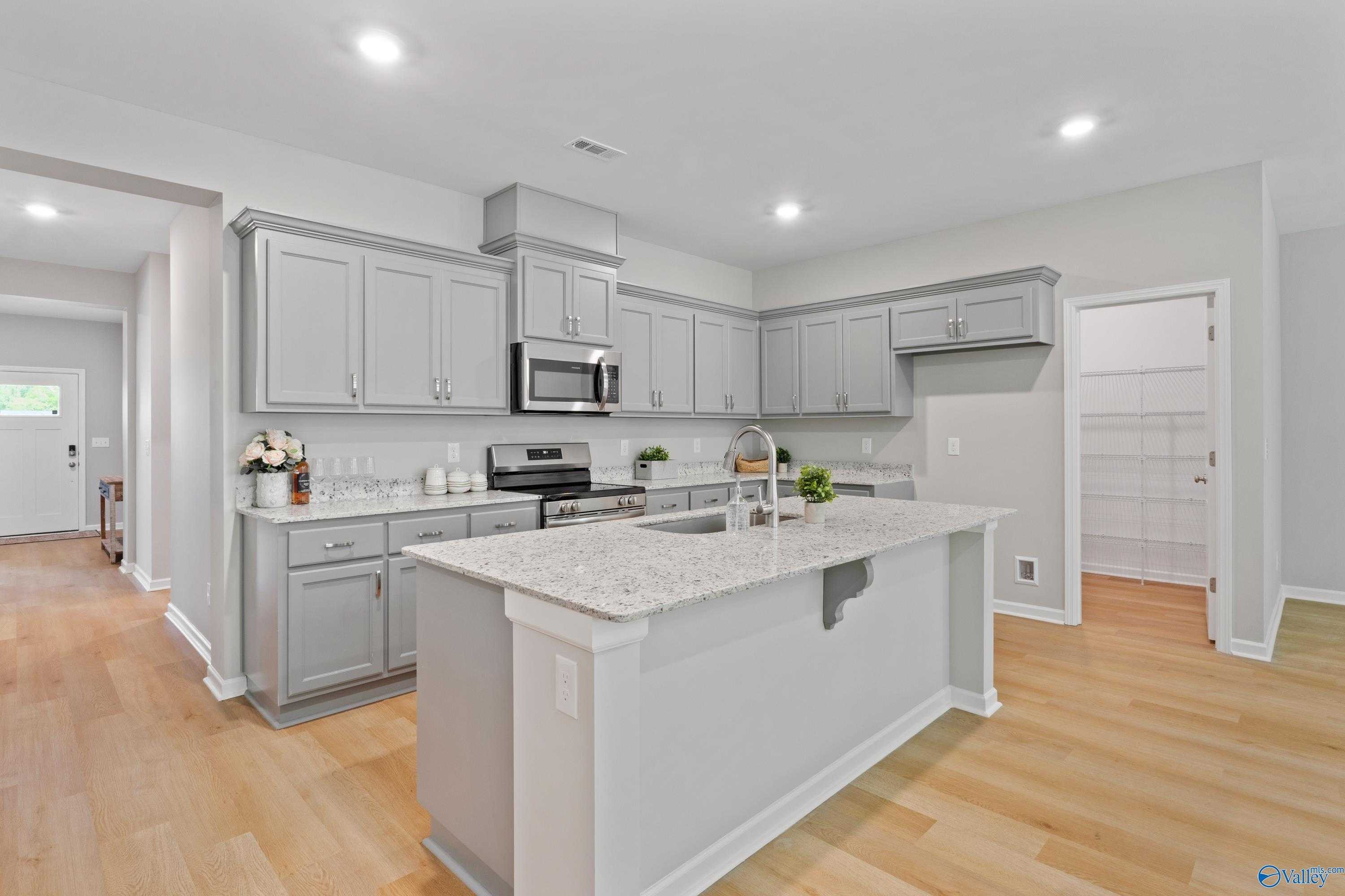 Modern kitchen with gray cabinets, granite island sink, stainless appliances in The Luna 4-bedroom home, Hazel Green, Alabama