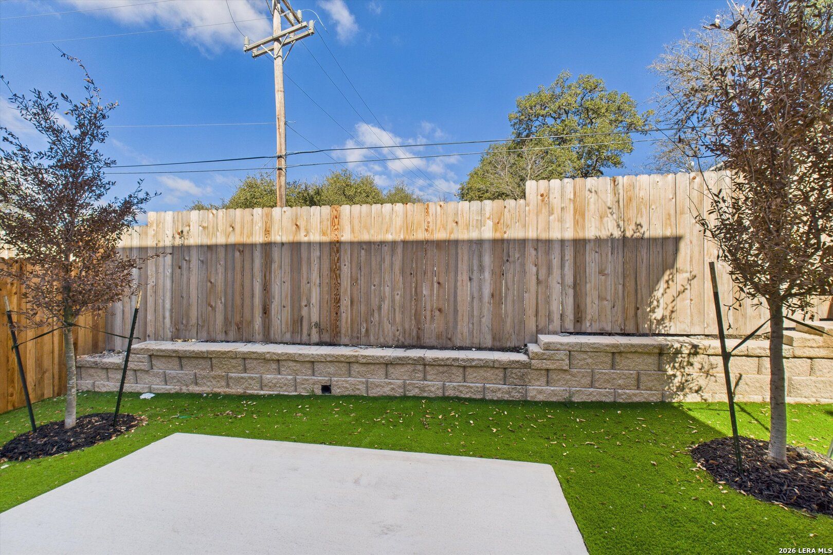 Private backyard with cedar privacy fence, green lawn, stone patio, and shade trees in The Gillian B, Meadows at Oak Creek, San Antonio