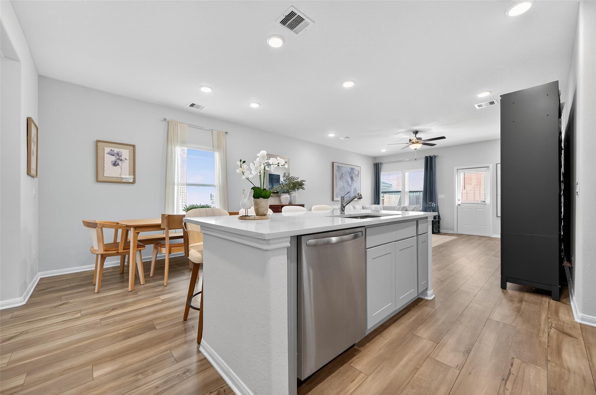 Bright open-concept kitchen with white island, stainless dishwasher, orchids, and dining table in Davidson Homes The Brazos E, Magnolia Texas